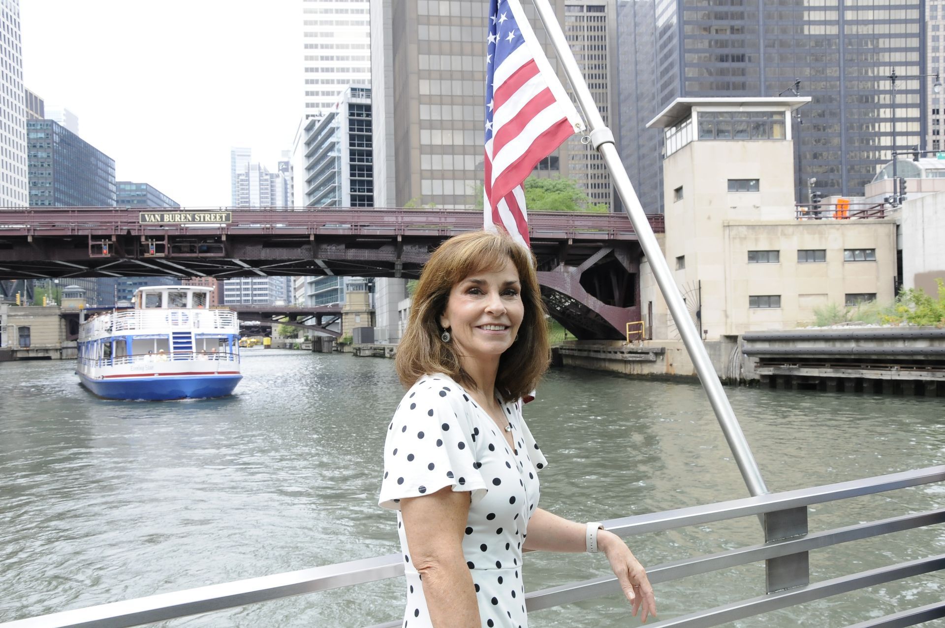 A woman in a polka dot dress stands on a bridge over a river
