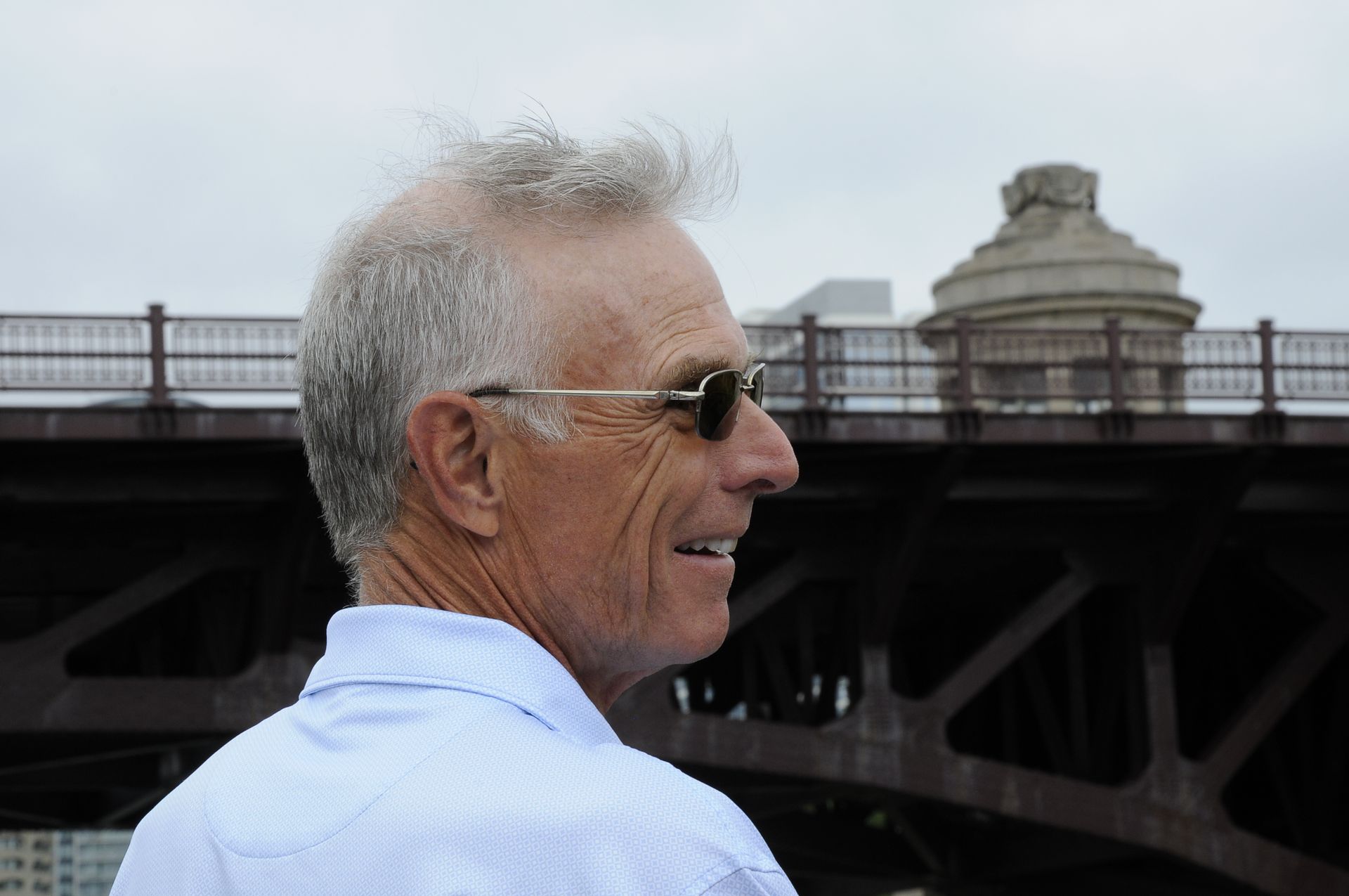 A man wearing sunglasses is standing in front of a bridge.