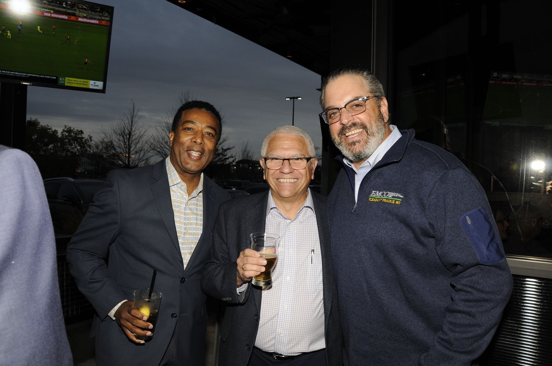 Three men are posing for a picture together while holding drinks.