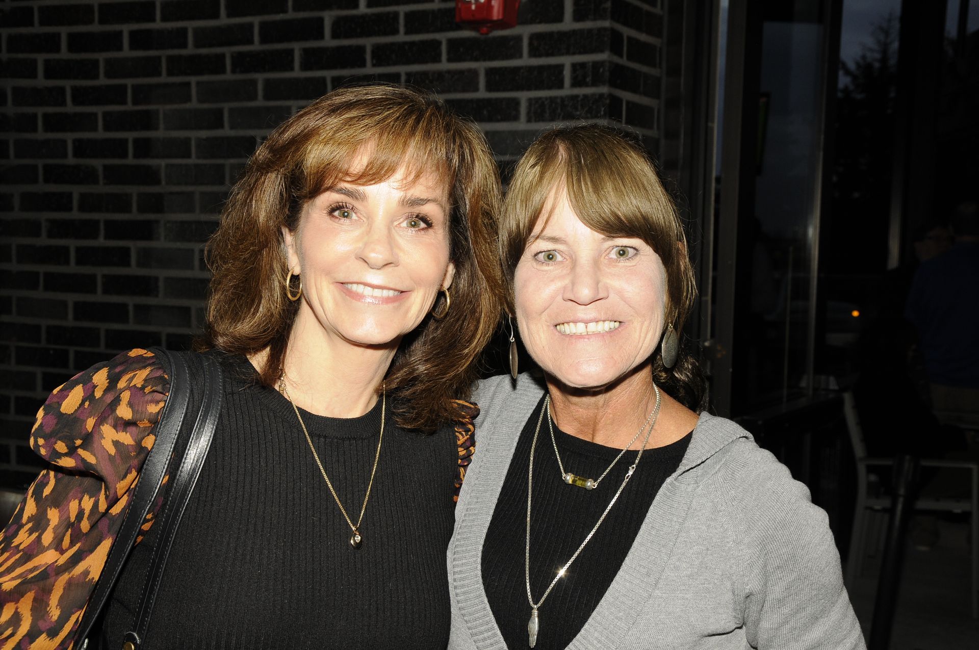 Two women are posing for a picture in front of a brick wall.