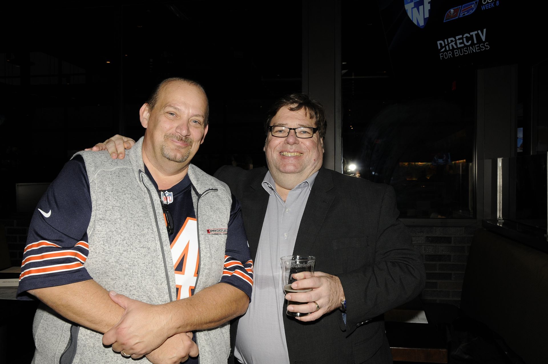 Two men are posing for a picture in front of a directv sign.
