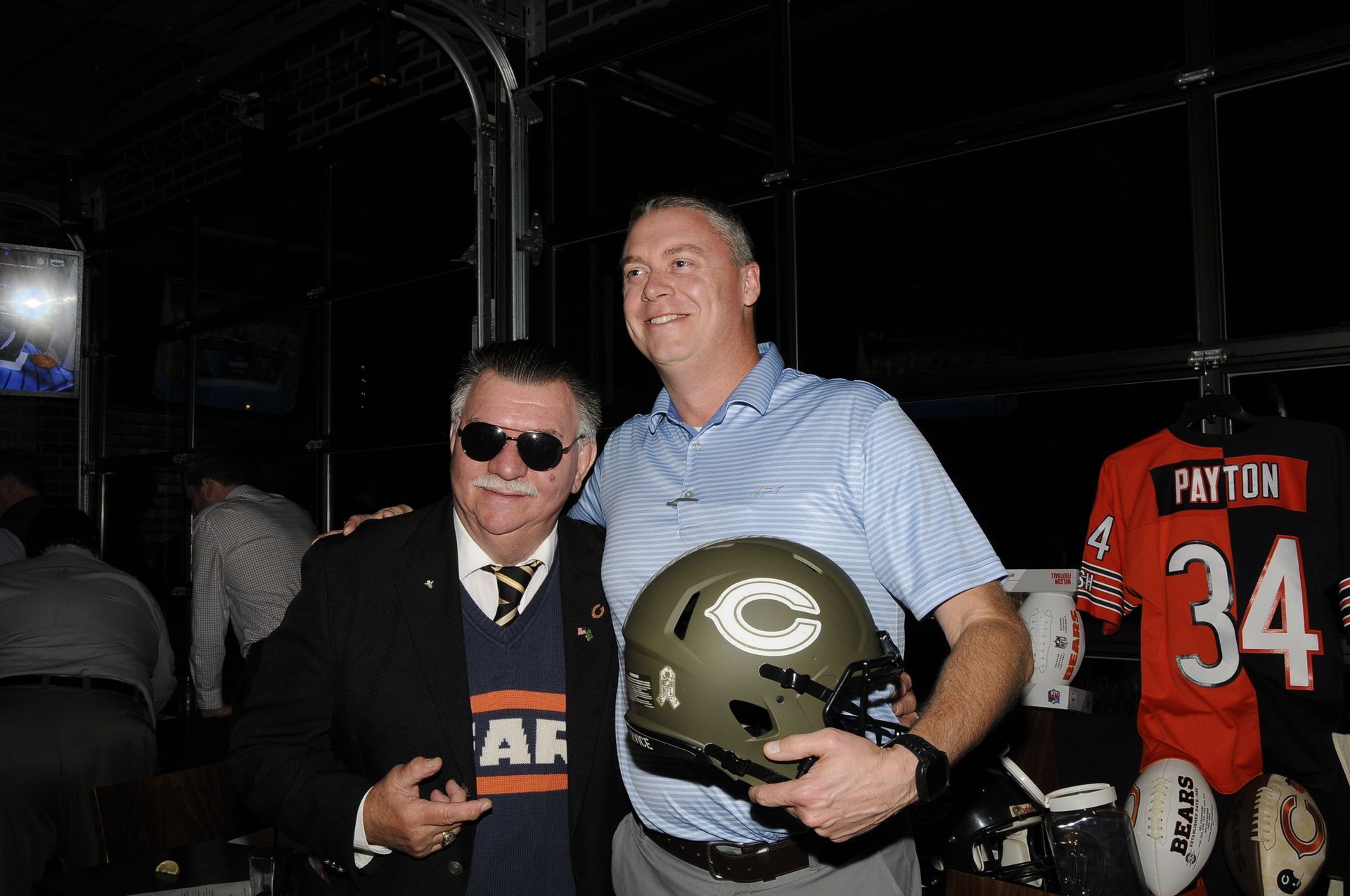 Two men standing next to each other holding a football helmet and a jersey with the number 34 on it