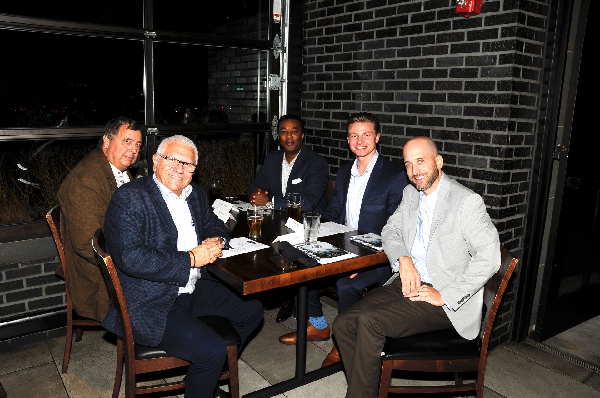 A group of men are sitting at a table in front of a brick wall.