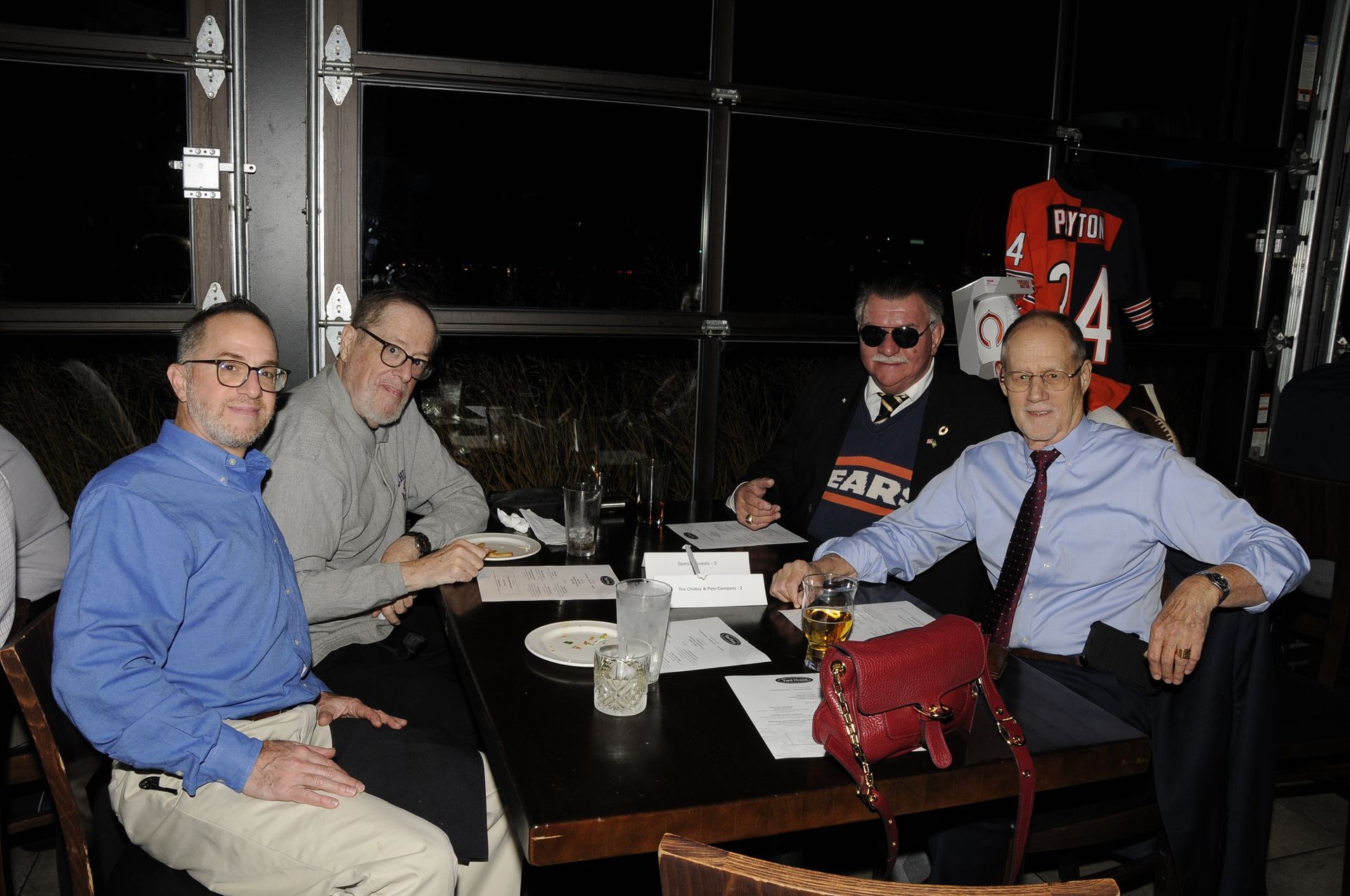 Four men are sitting at a table with one wearing a bears shirt