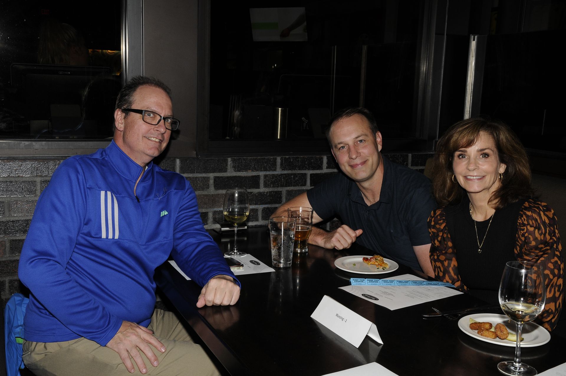 Three people are sitting at a table with plates of food and wine glasses.