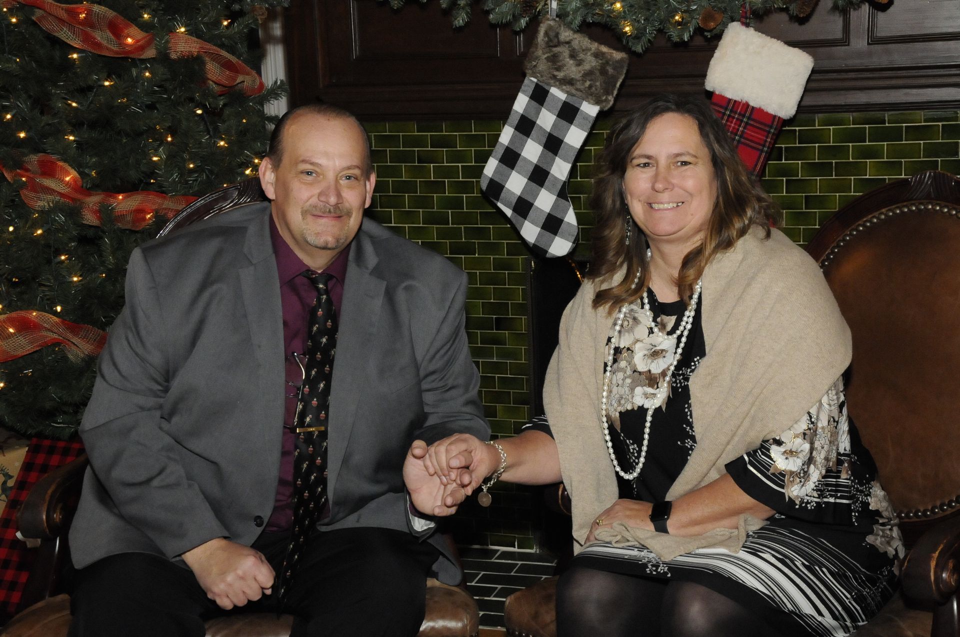 A man and a woman are sitting on a couch holding hands in front of a christmas tree.
