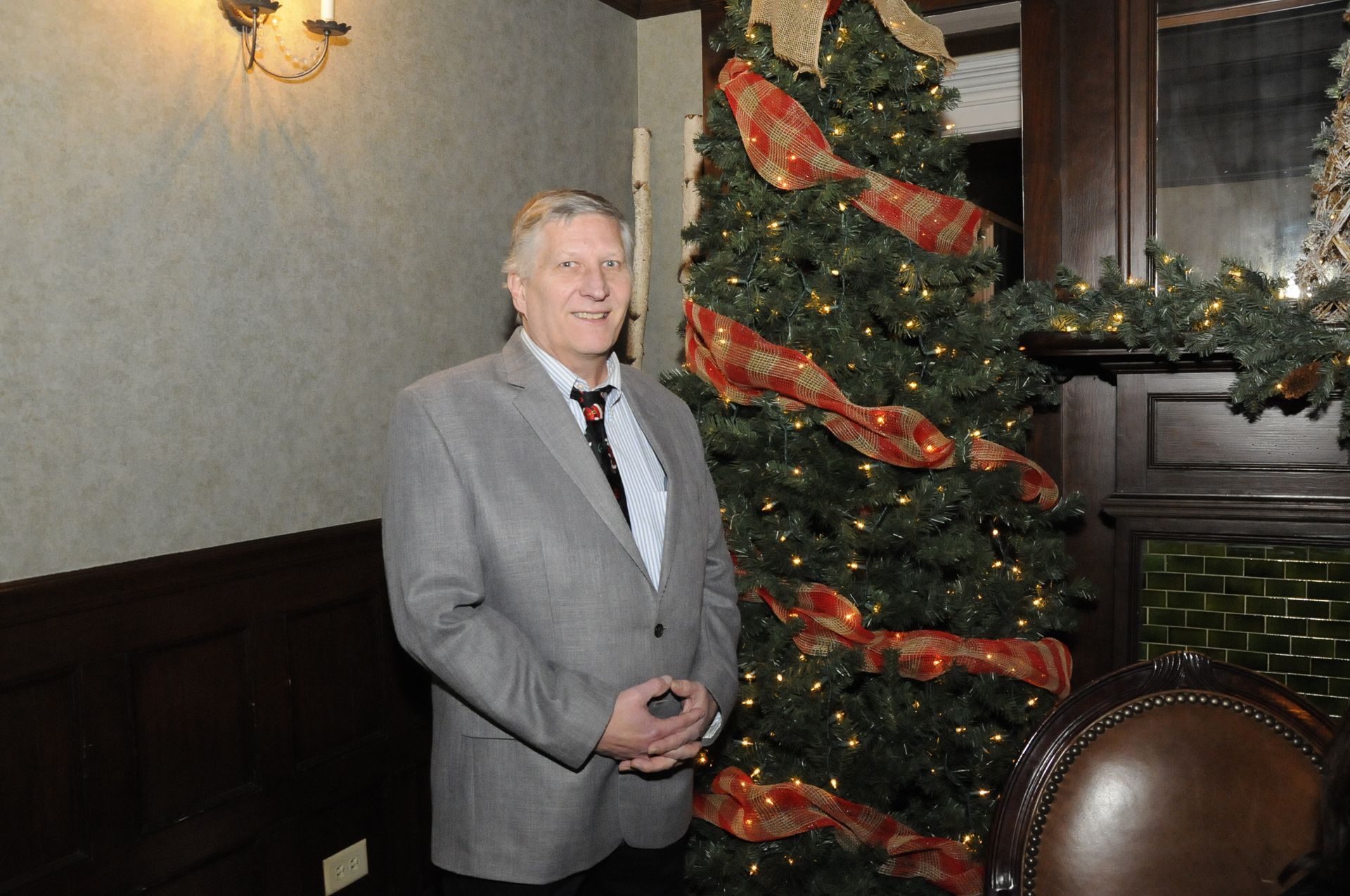 A man in a suit and tie is standing in front of a christmas tree.