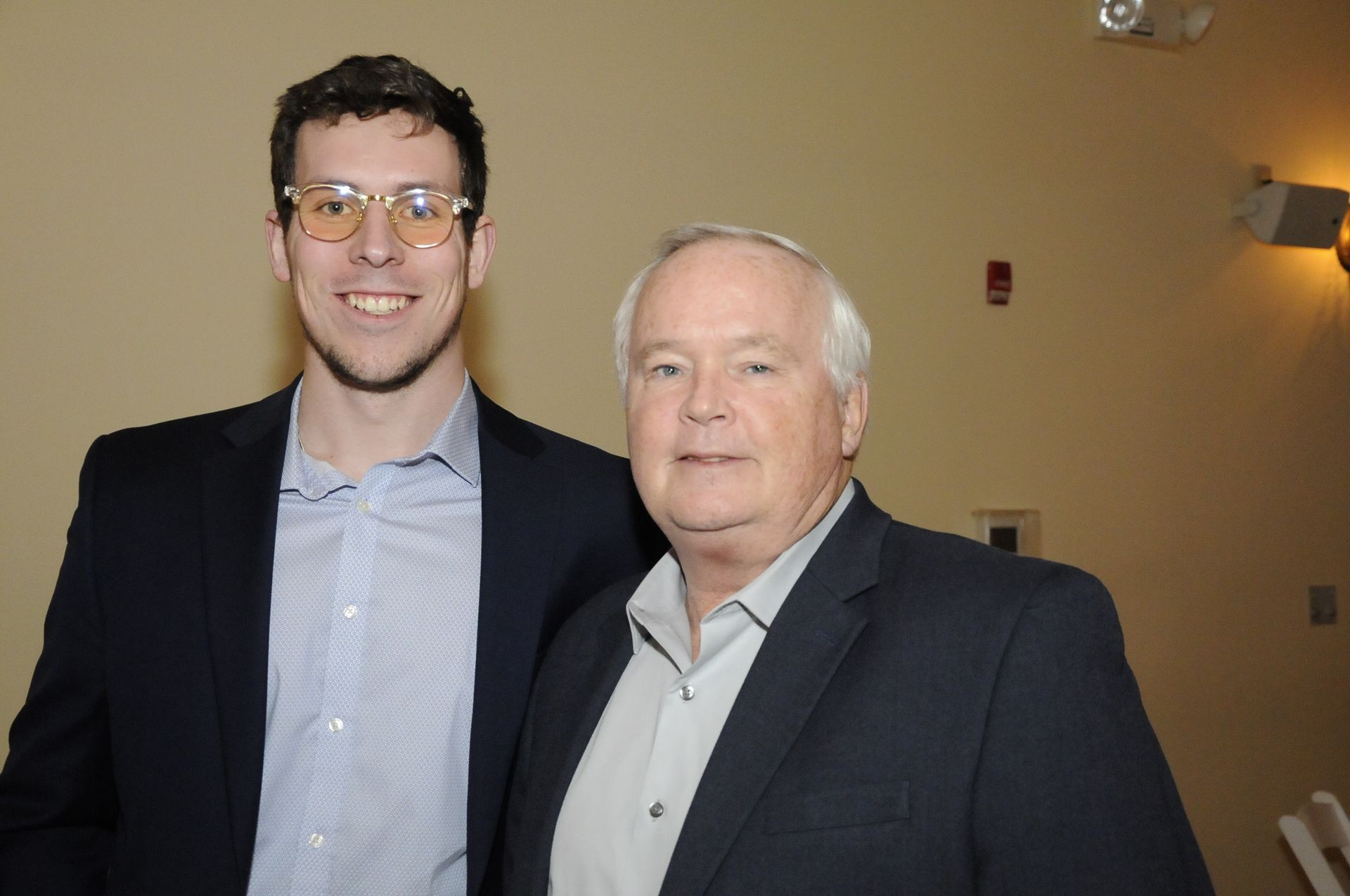 Two men in suits and glasses are posing for a picture.