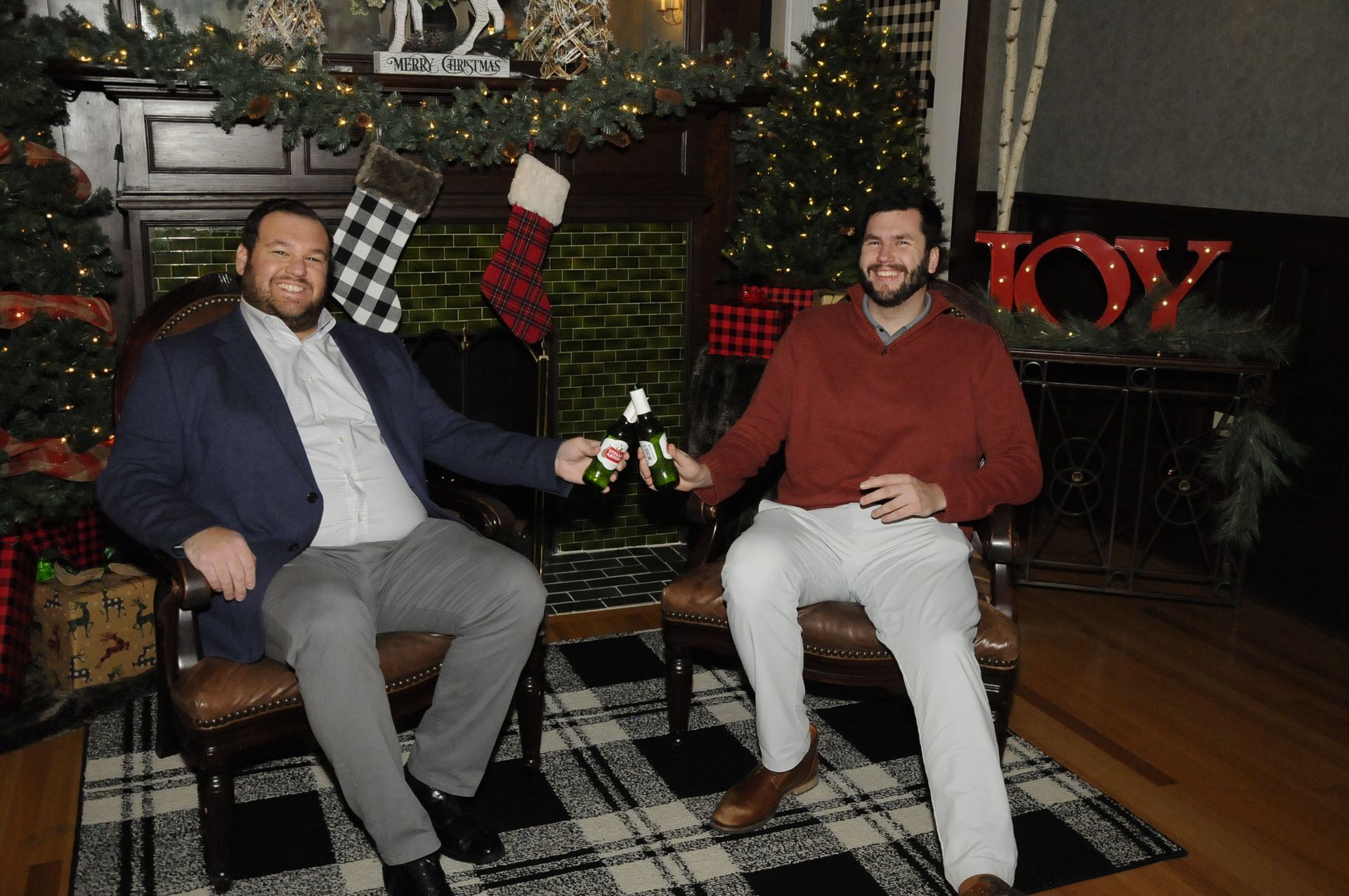 Two men are sitting in chairs in front of a christmas tree.