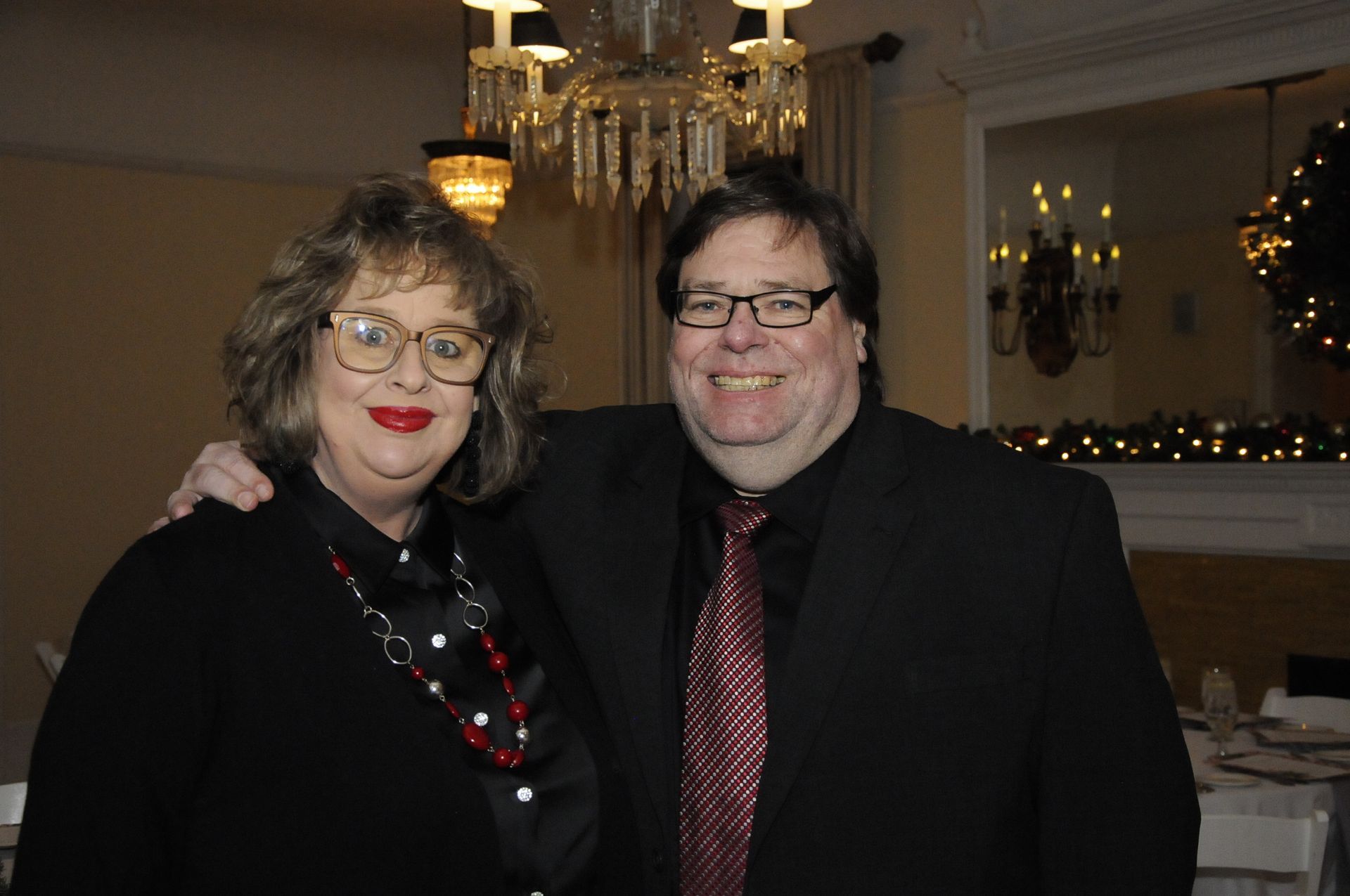 A man and a woman are posing for a picture in front of a chandelier.