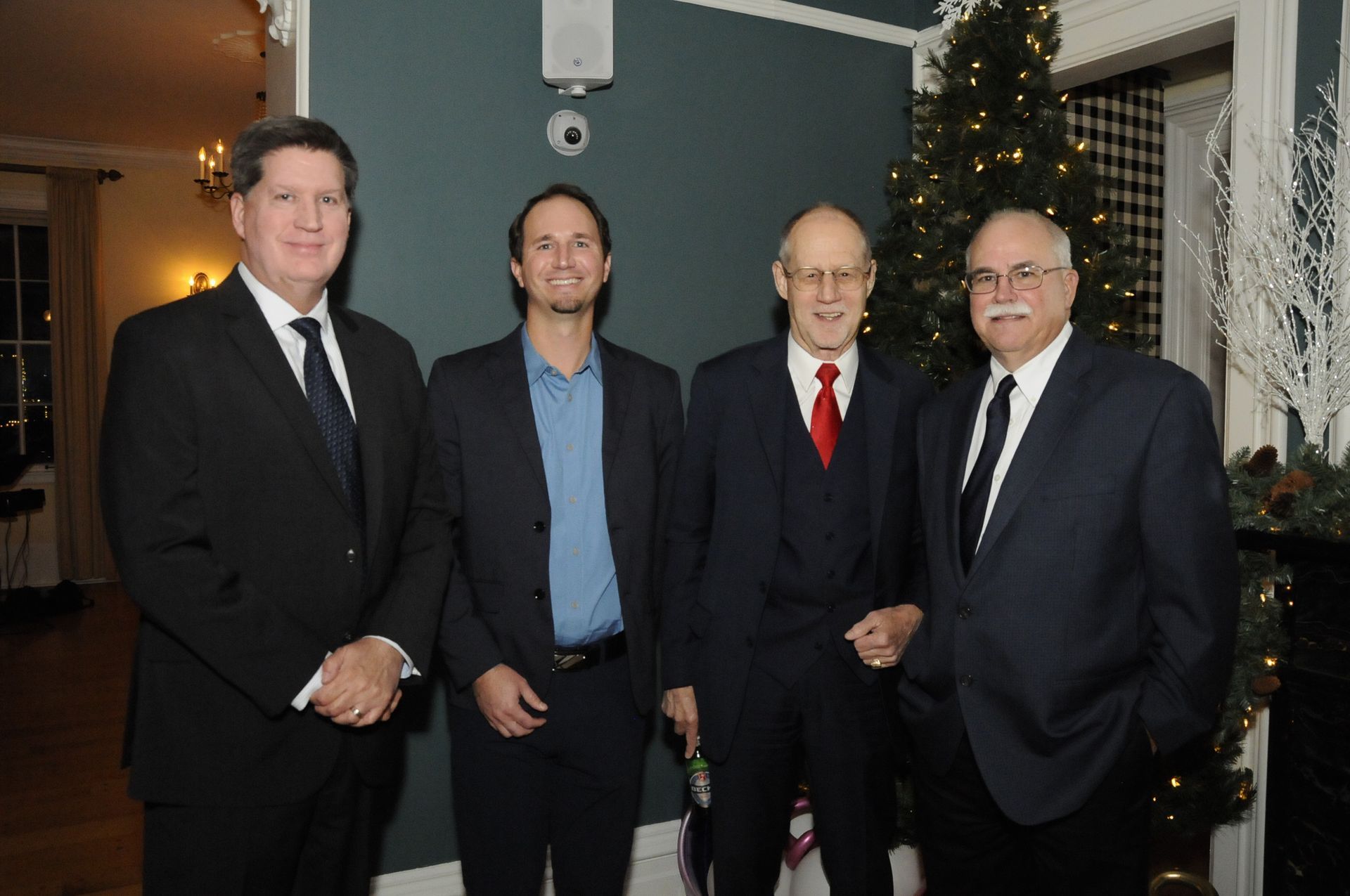 Four men are posing for a picture in front of a christmas tree
