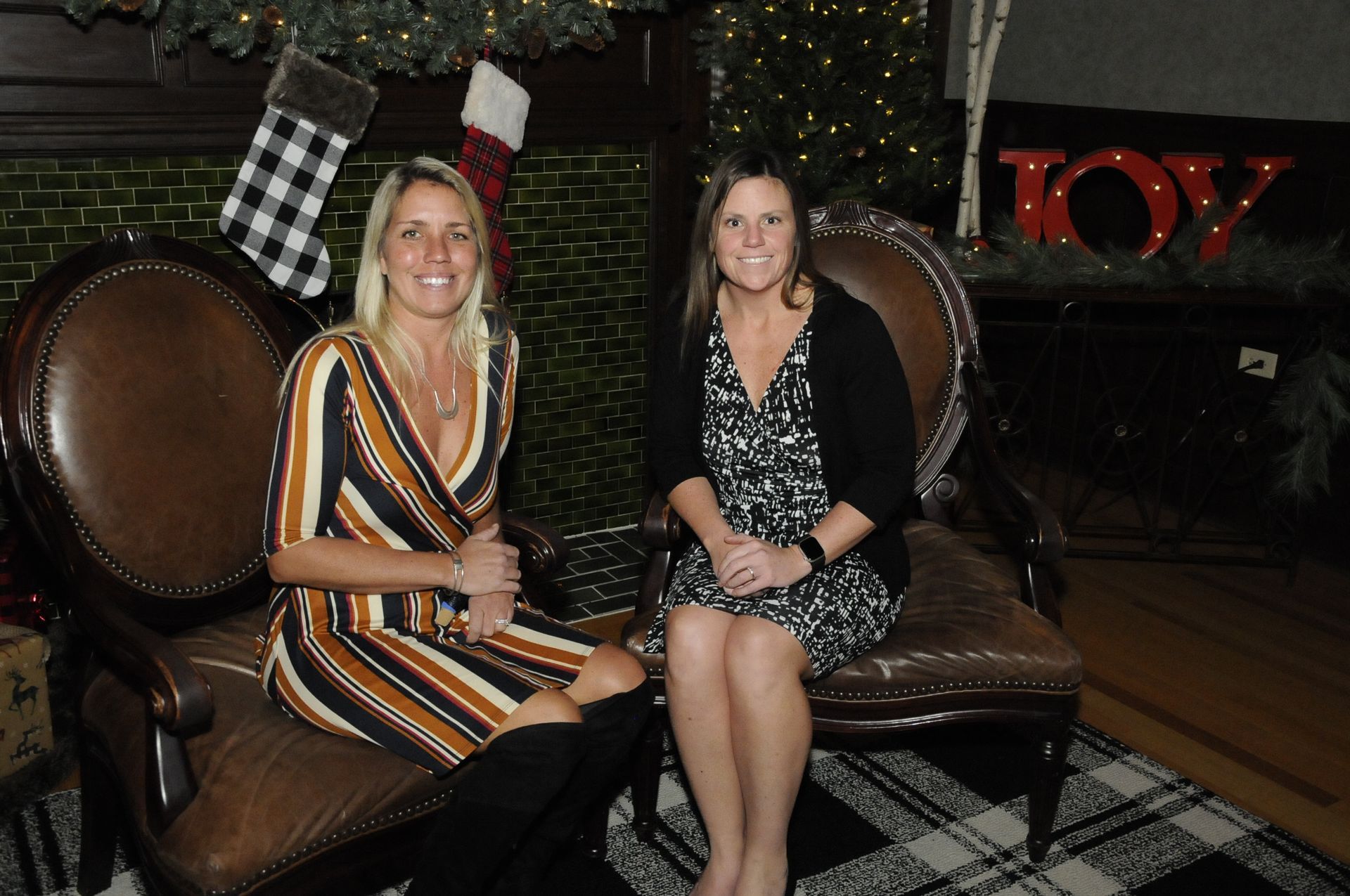 Two women are sitting in chairs in front of a fireplace.