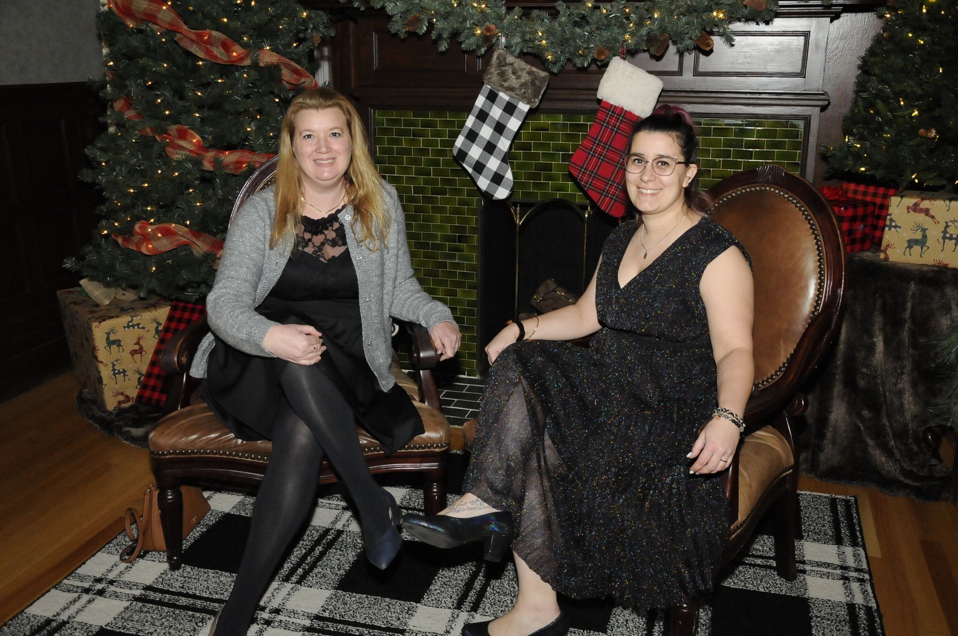 Two women are sitting next to each other in front of a christmas tree.