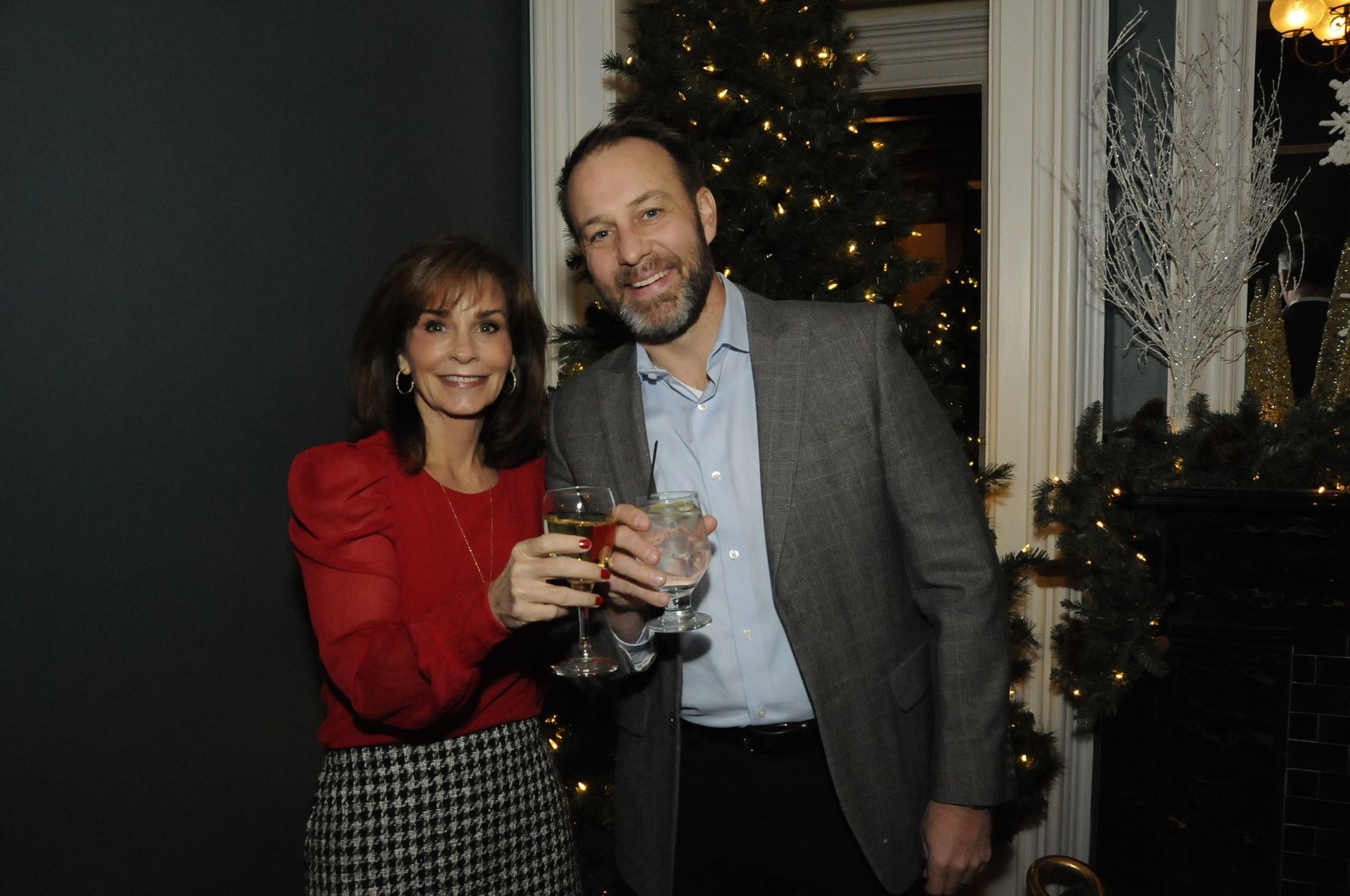 A man and a woman are toasting with wine glasses in front of a christmas tree.