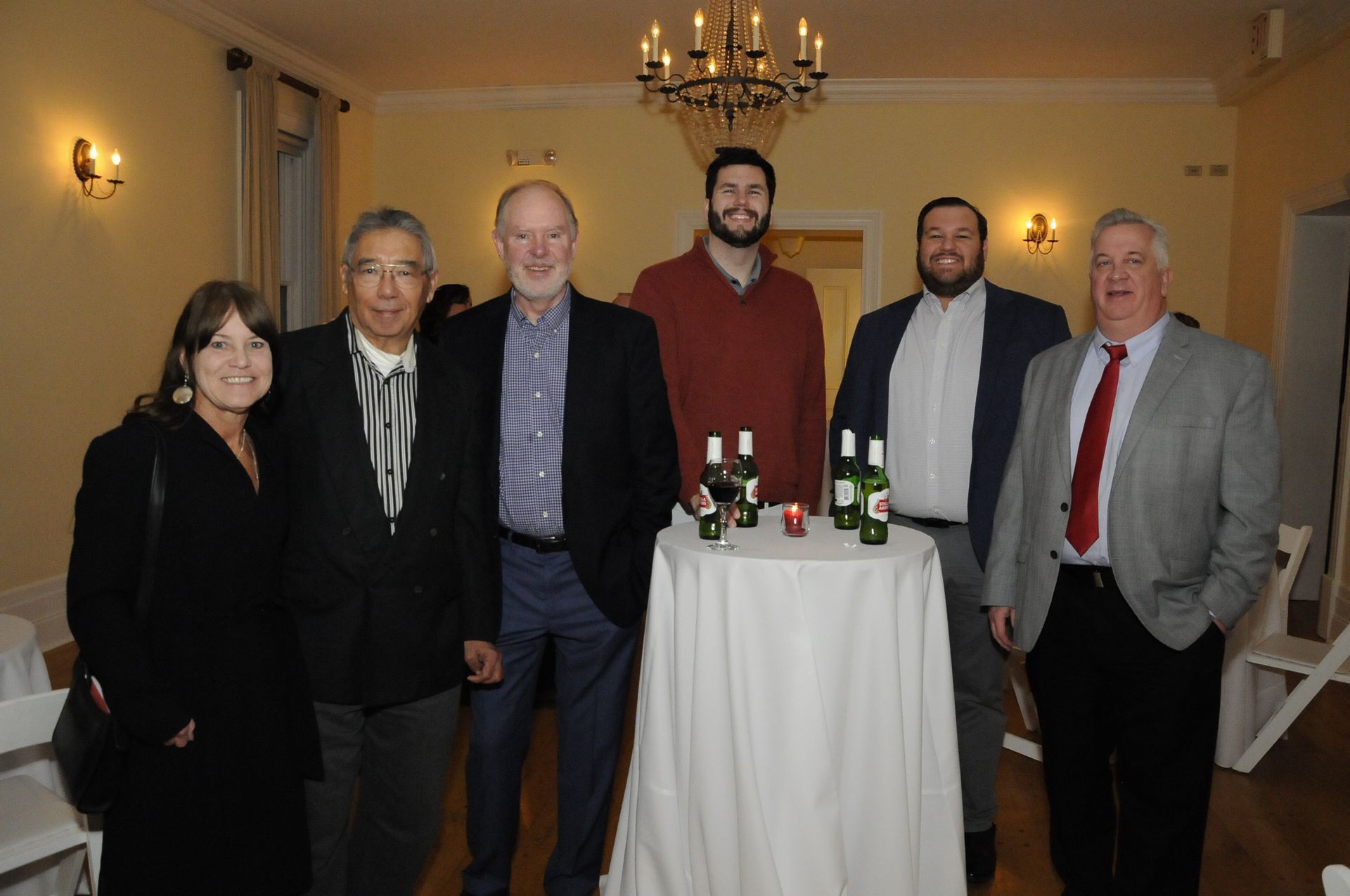A group of people standing around a table with bottles of beer on it.
