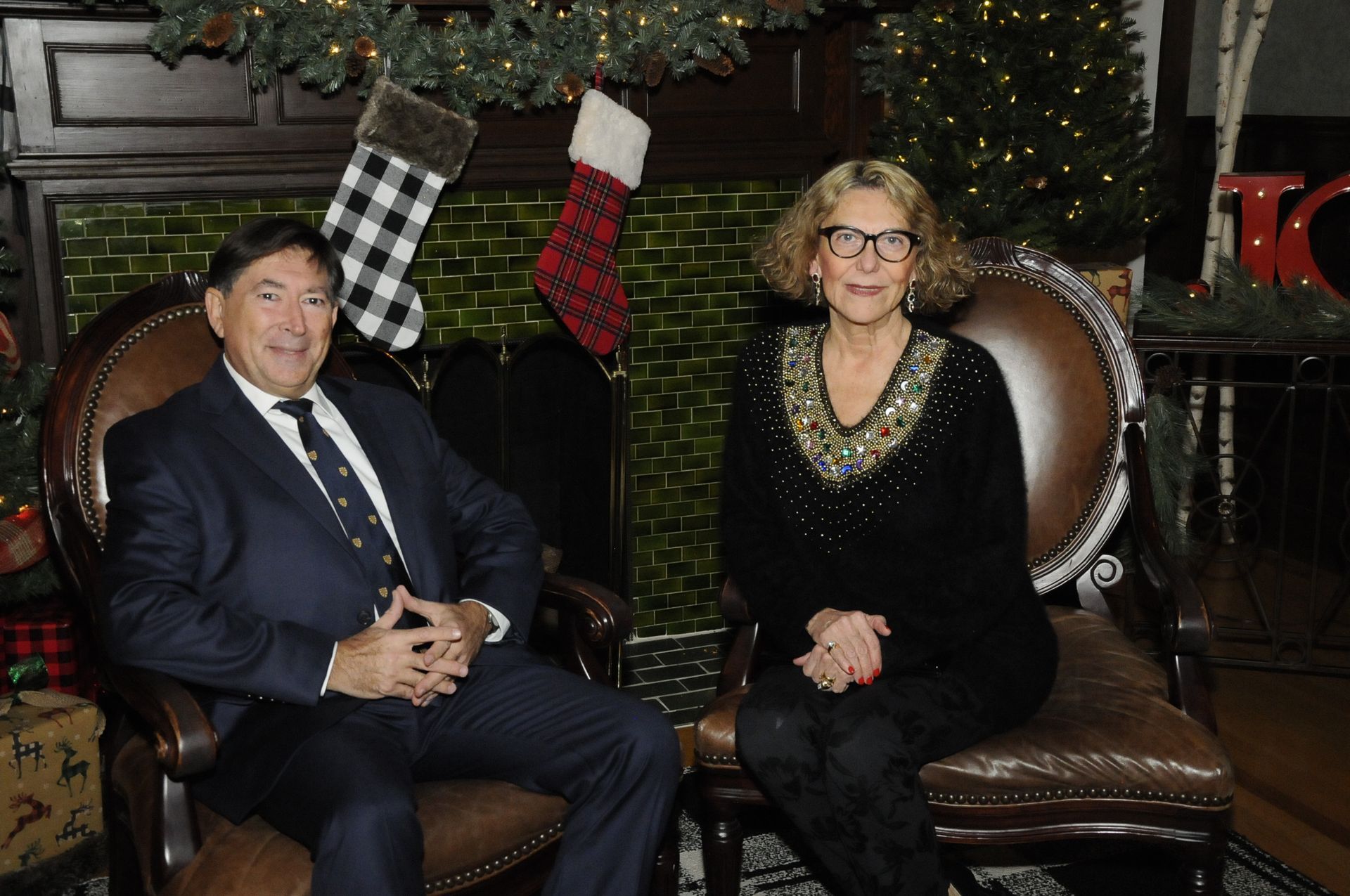 A man and a woman are sitting in chairs in front of a fireplace.