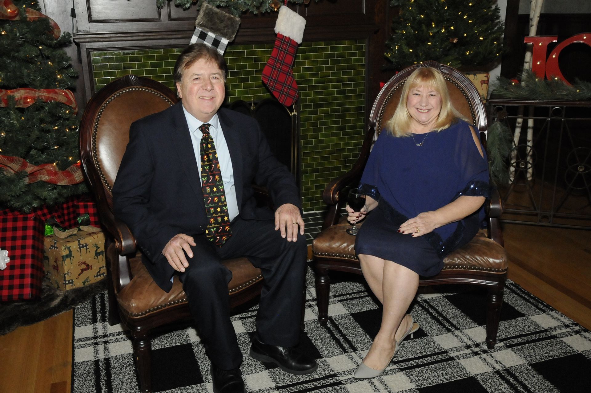 A man and a woman are sitting in chairs in front of a christmas tree.