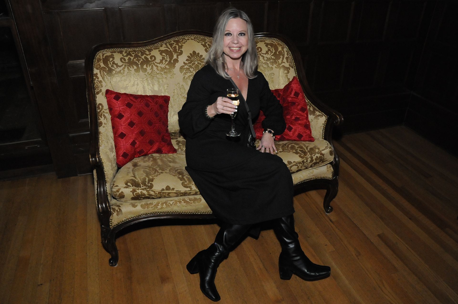 A woman in a black dress is sitting on a couch holding a glass of wine