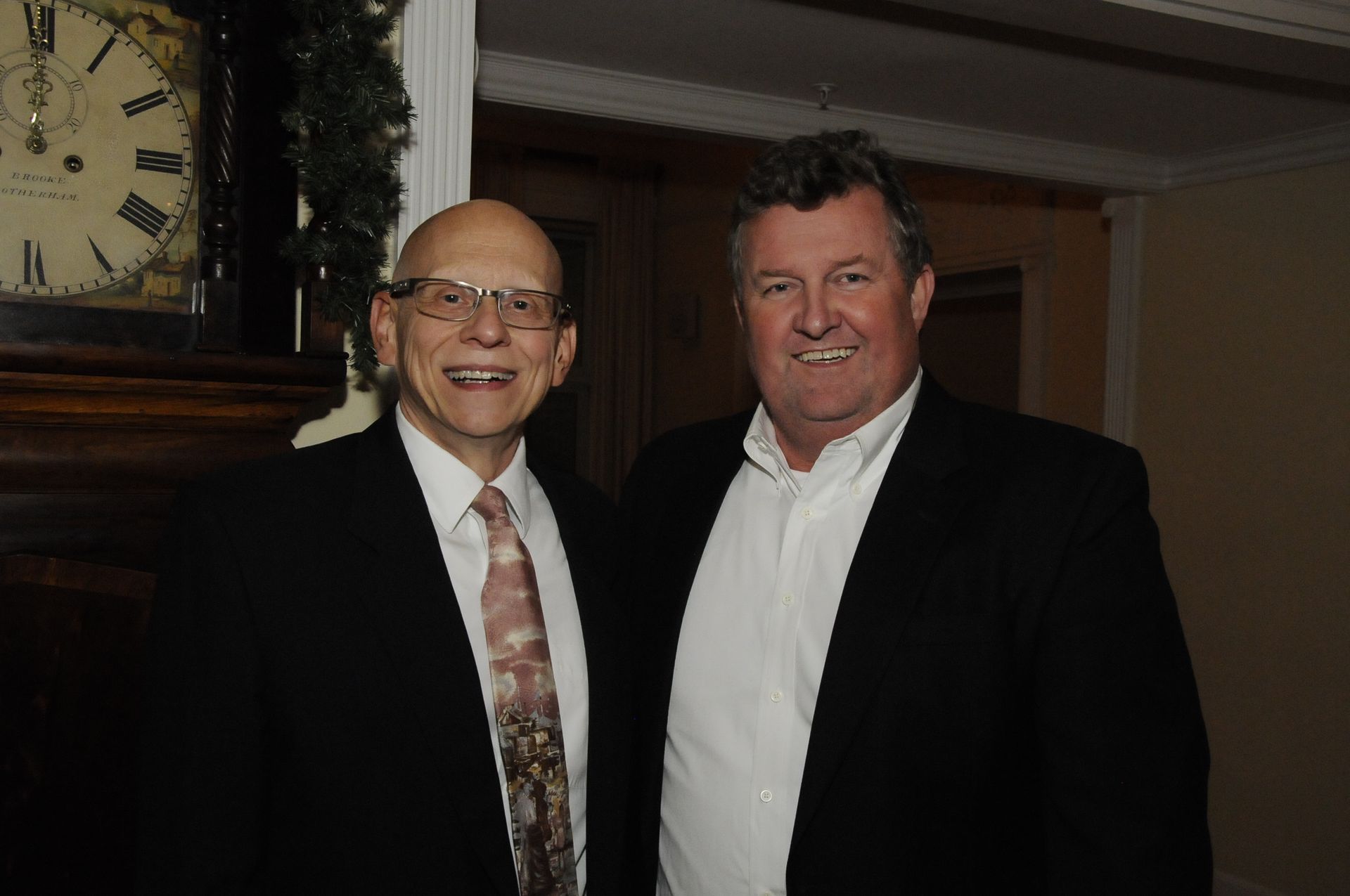 Two men are posing for a picture in front of a clock.