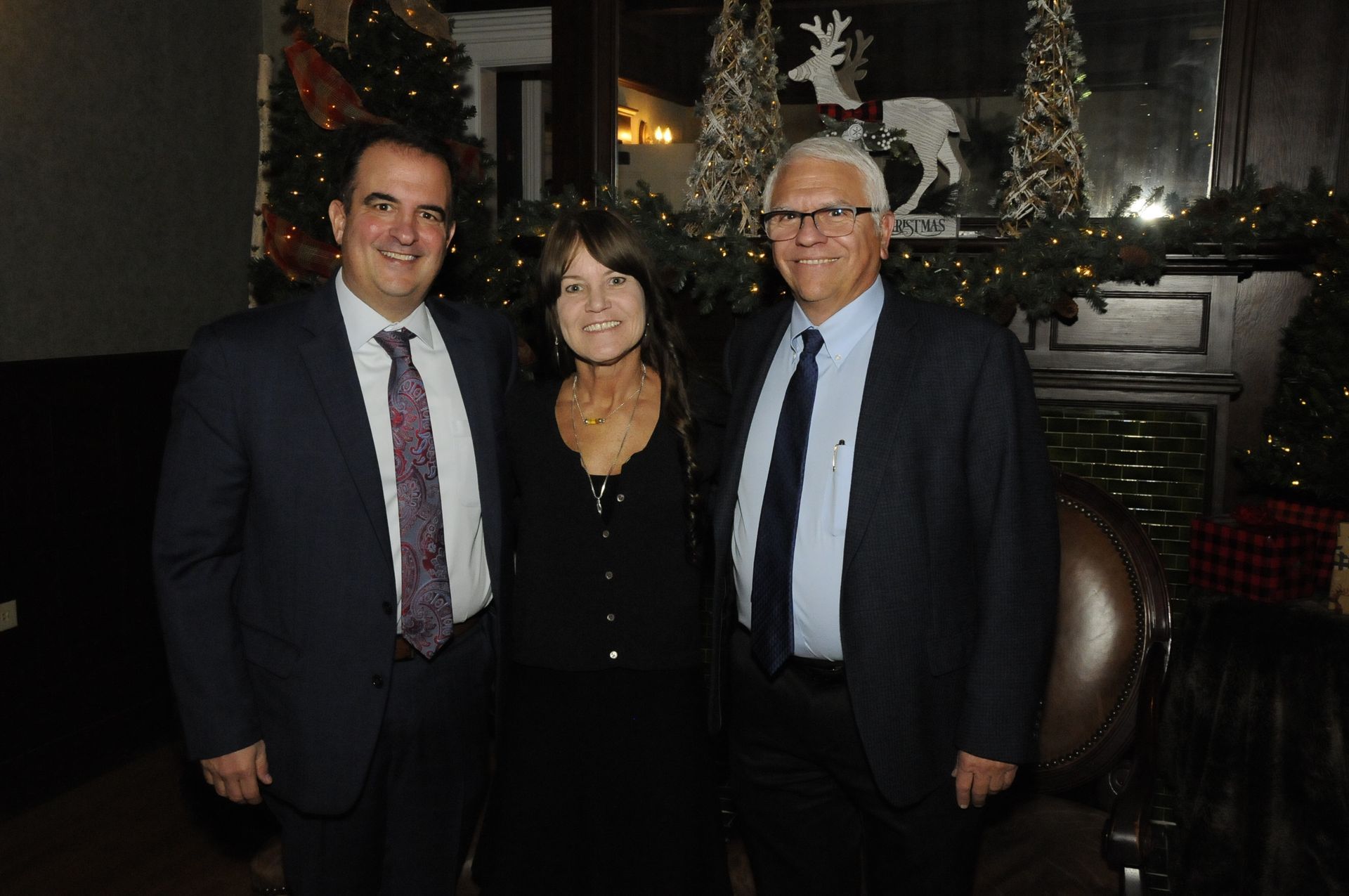 Two men and a woman are posing for a picture in front of a christmas tree