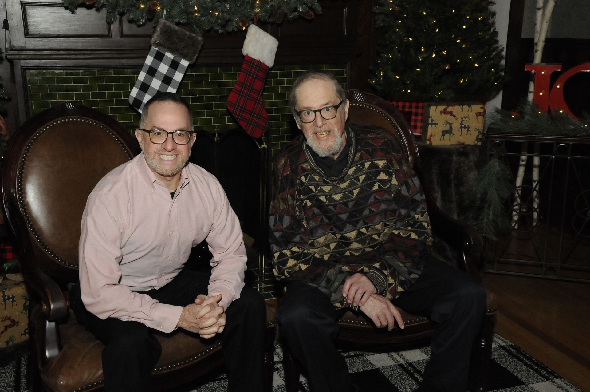 Two men are sitting on a couch in front of a christmas tree.