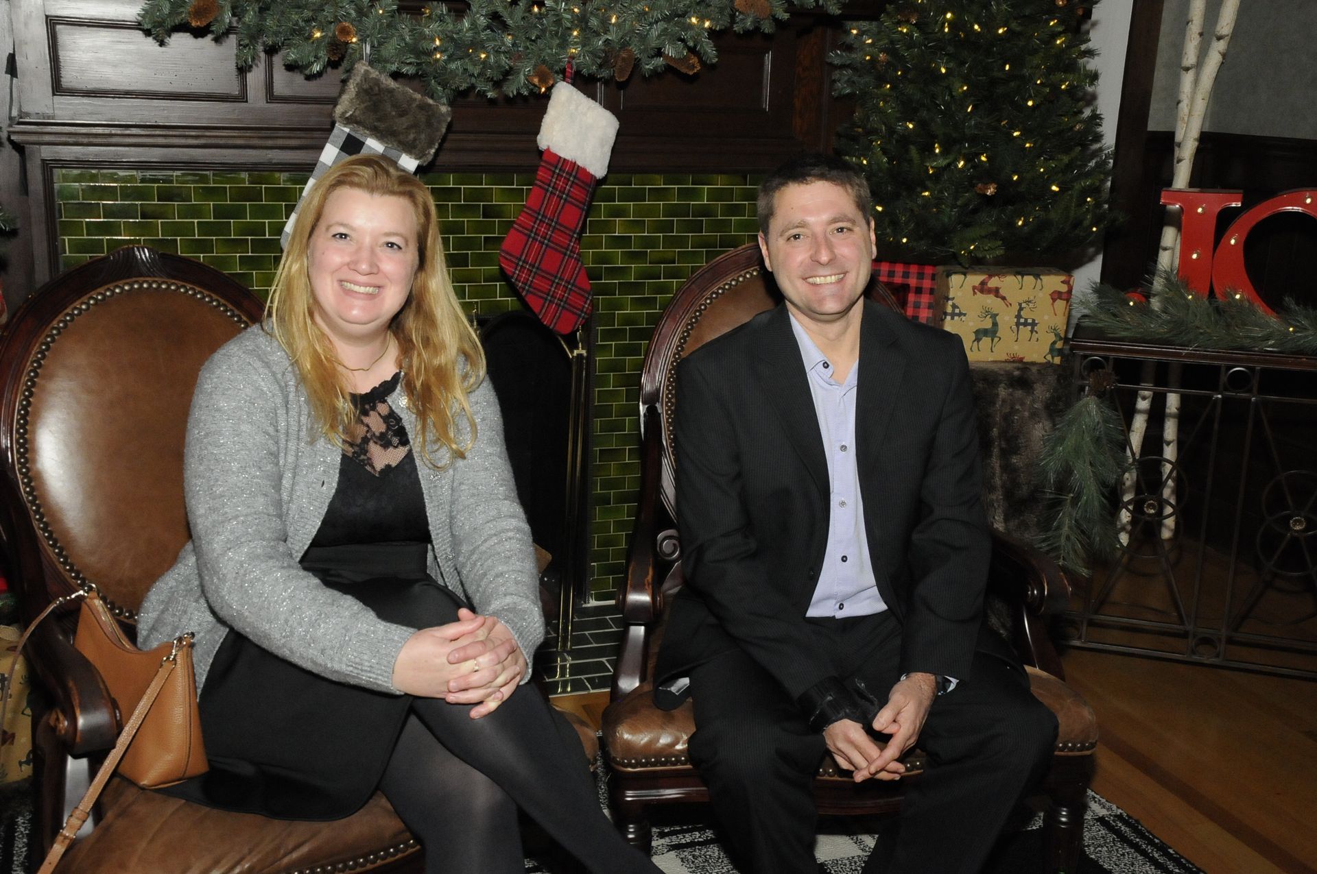 A man and a woman are sitting in chairs in front of a christmas tree.