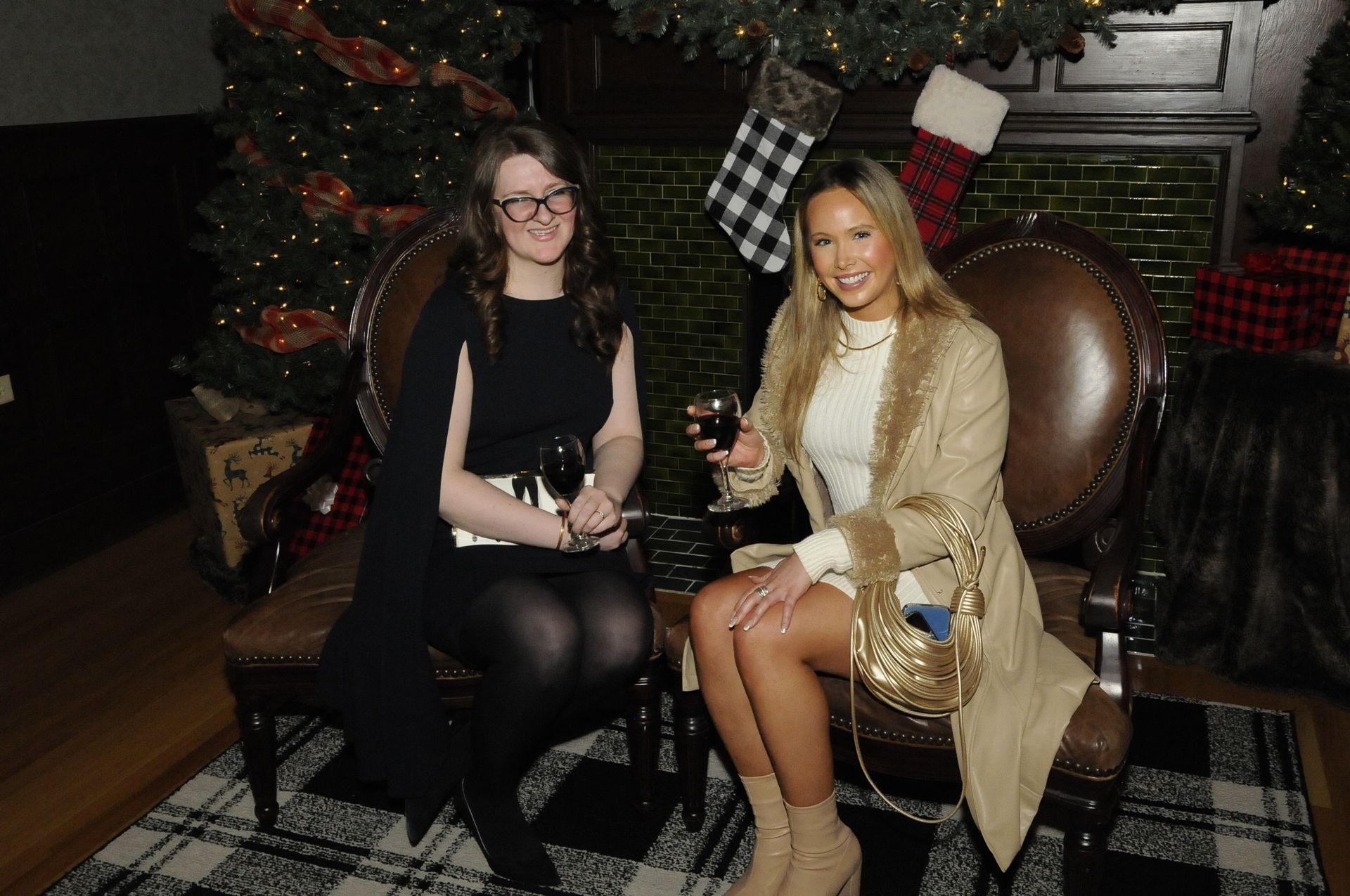 Two women are sitting next to each other in front of a christmas tree.