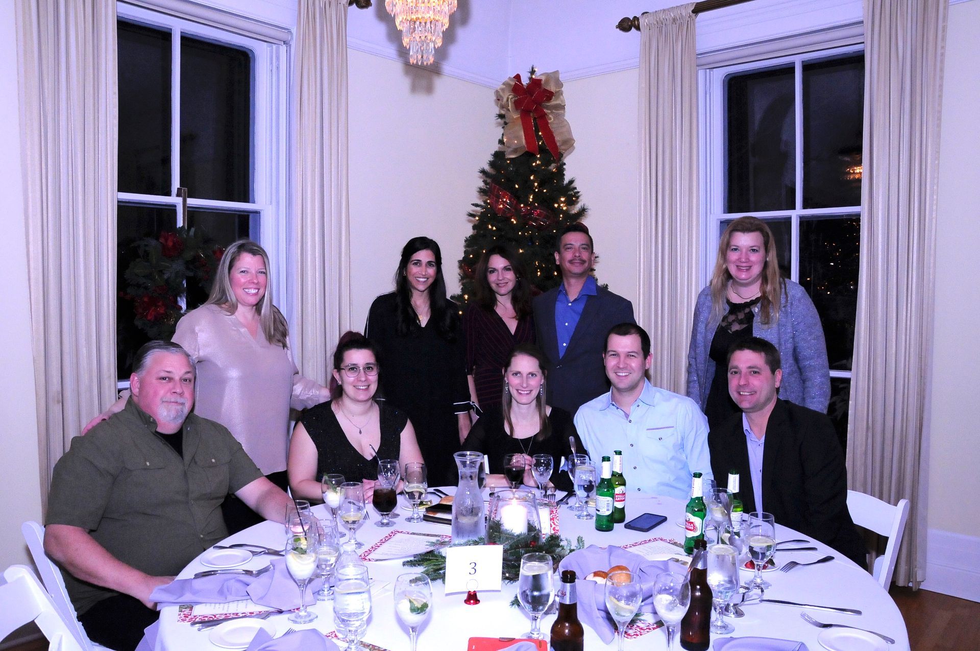 A group of people are sitting around a table with a christmas tree in the background.