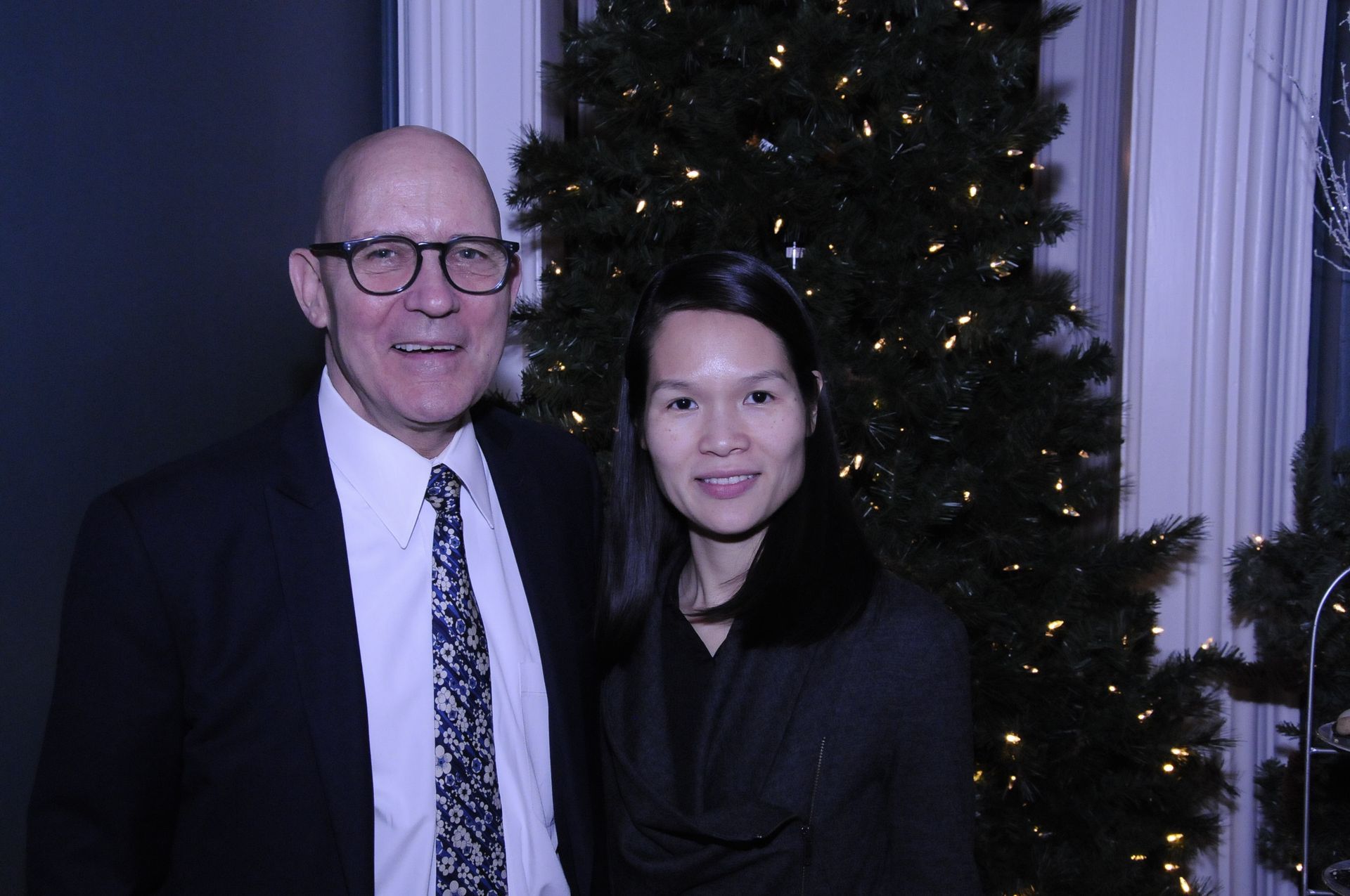 A man and a woman are posing for a picture in front of a christmas tree.