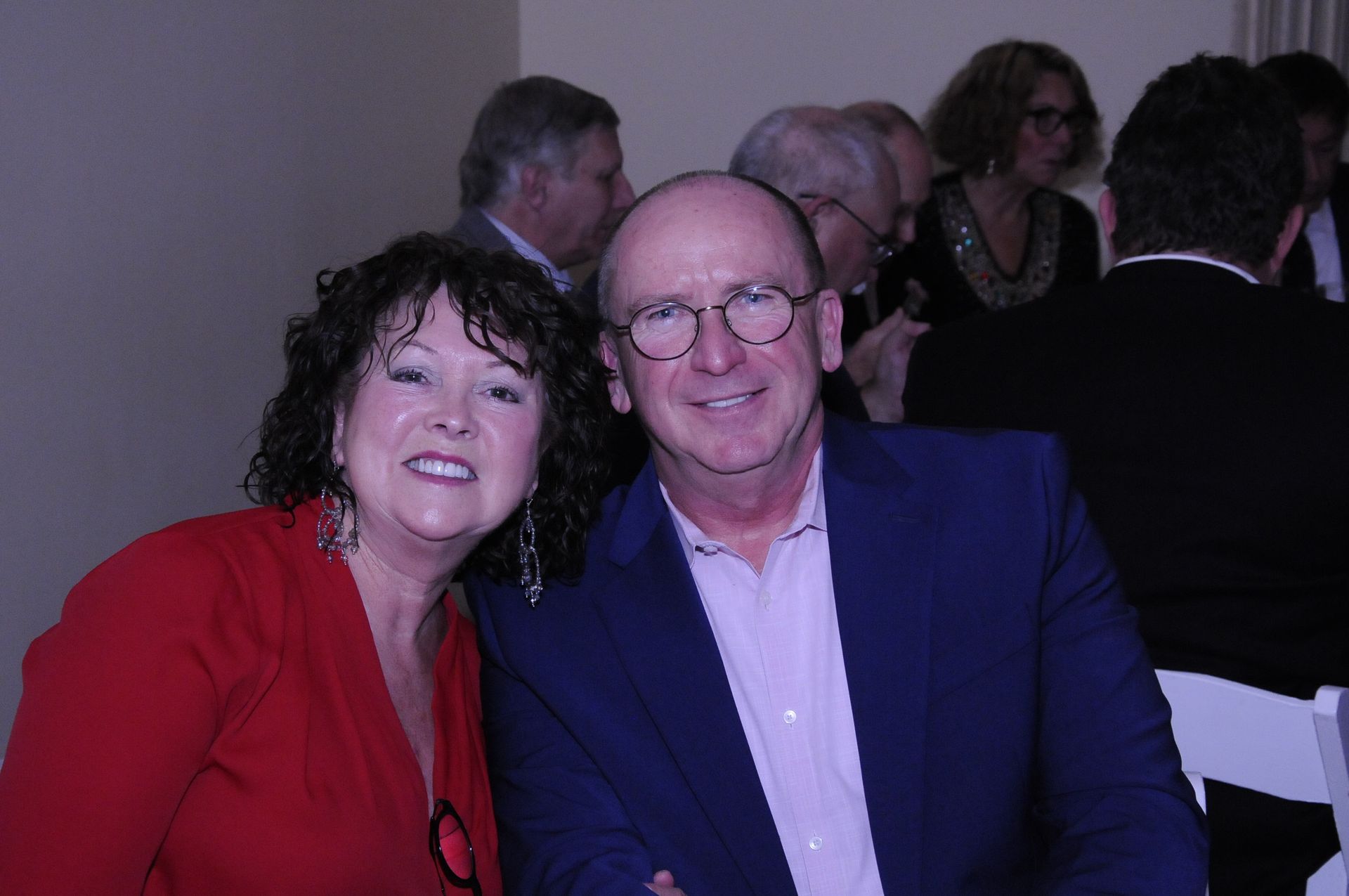 A man and a woman are posing for a picture in a crowded room.