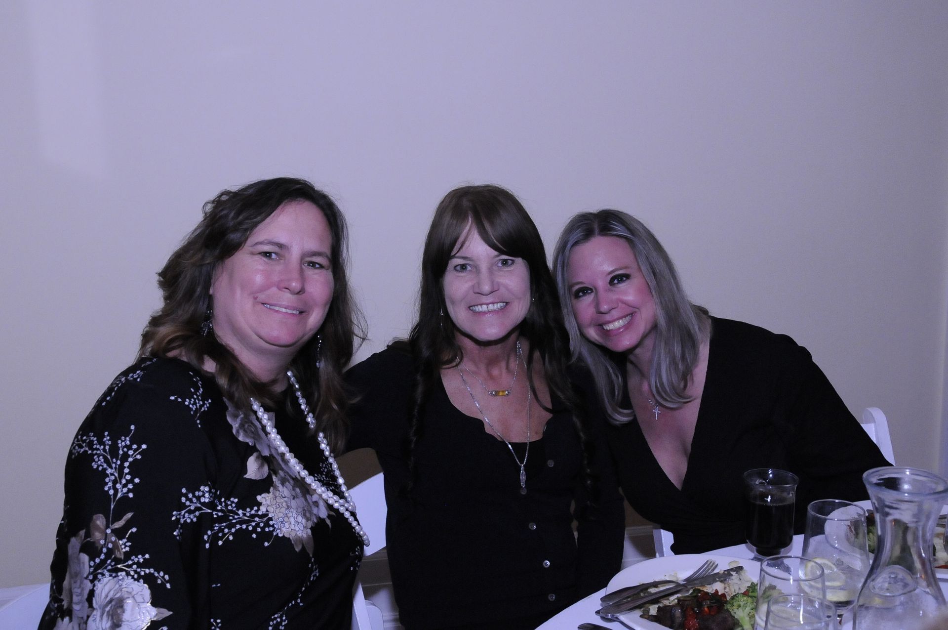 Three women are posing for a picture while sitting at a table.