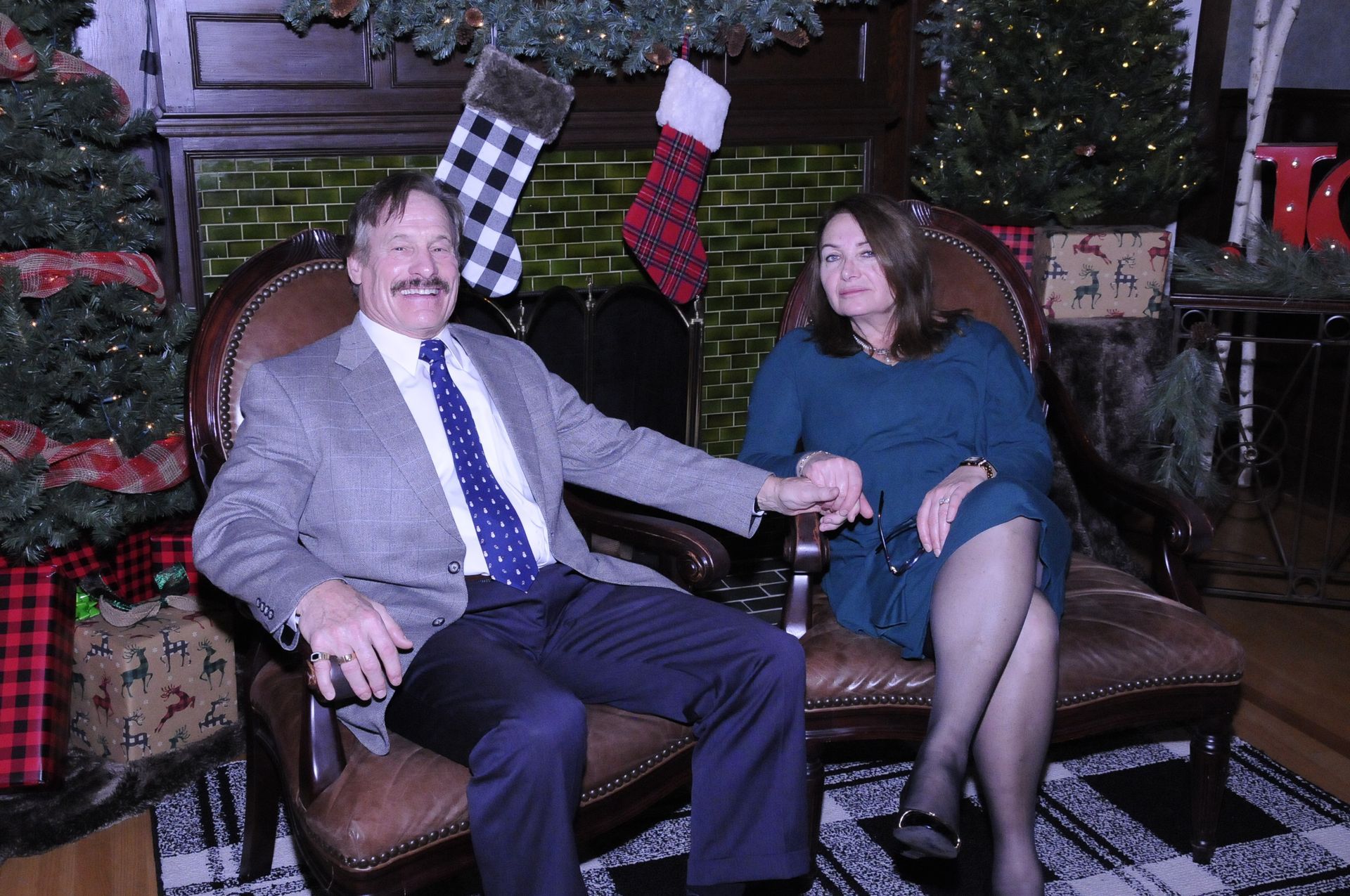 A man and a woman are sitting in chairs holding hands in front of a christmas tree.