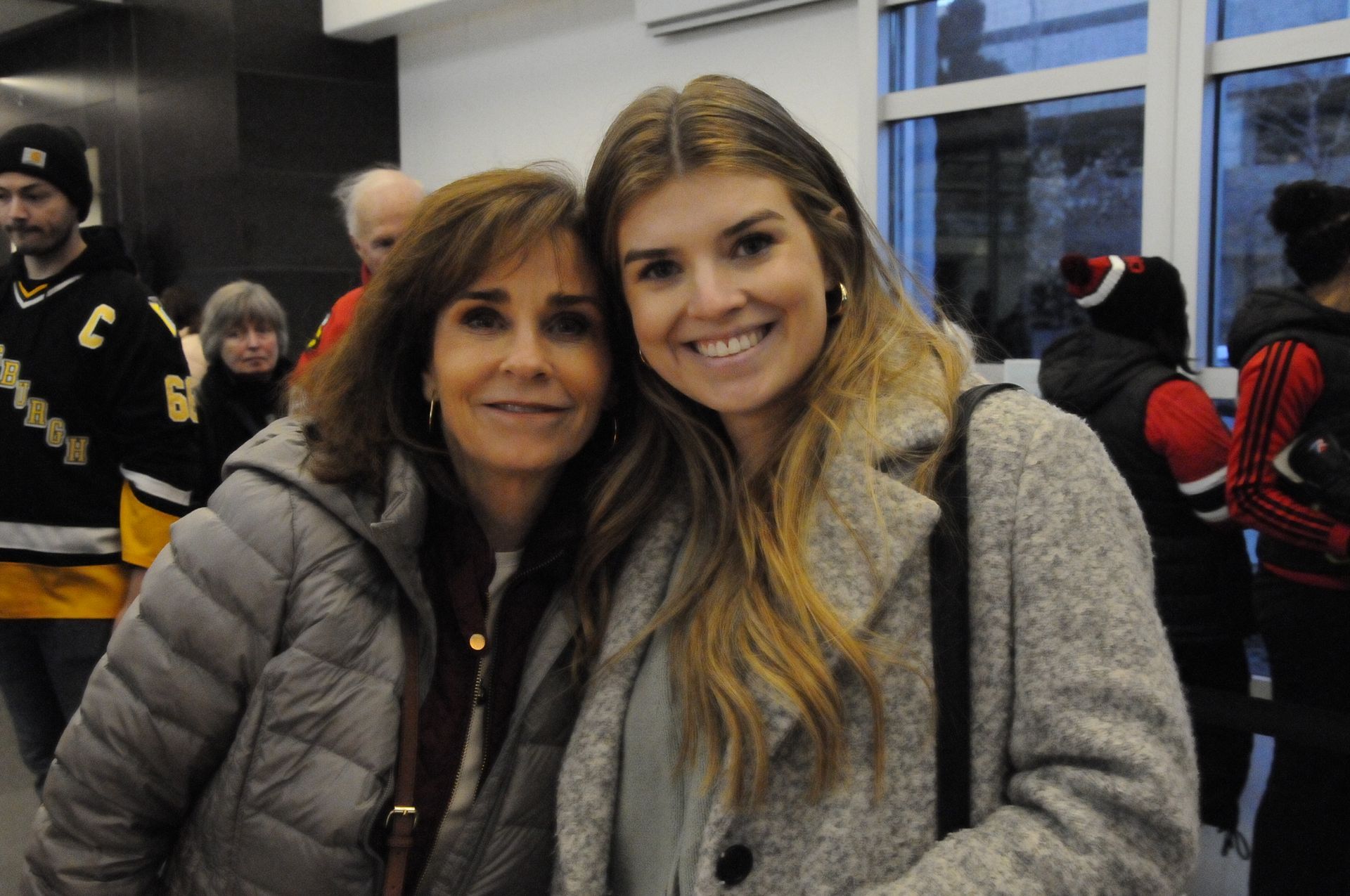 Two women are posing for a picture in front of a window.