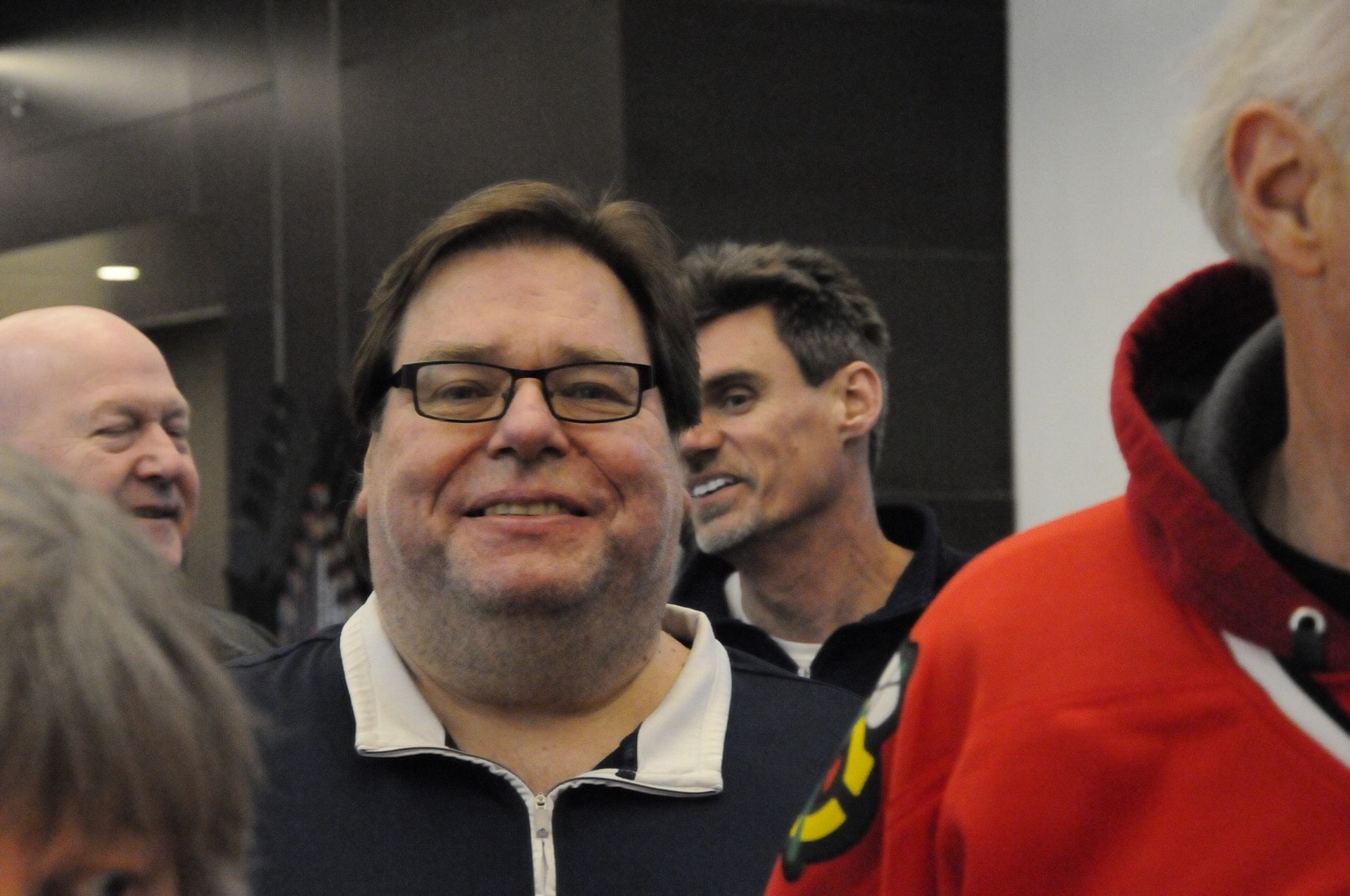 A man wearing glasses and a red hoodie smiles for the camera
