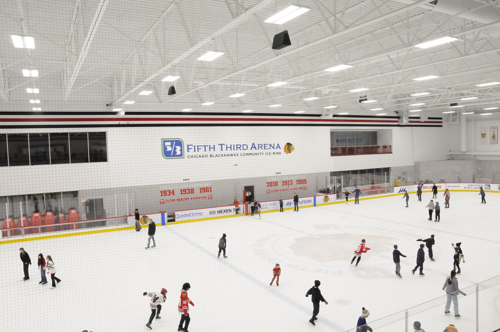 A group of people are ice skating in a large indoor rink.