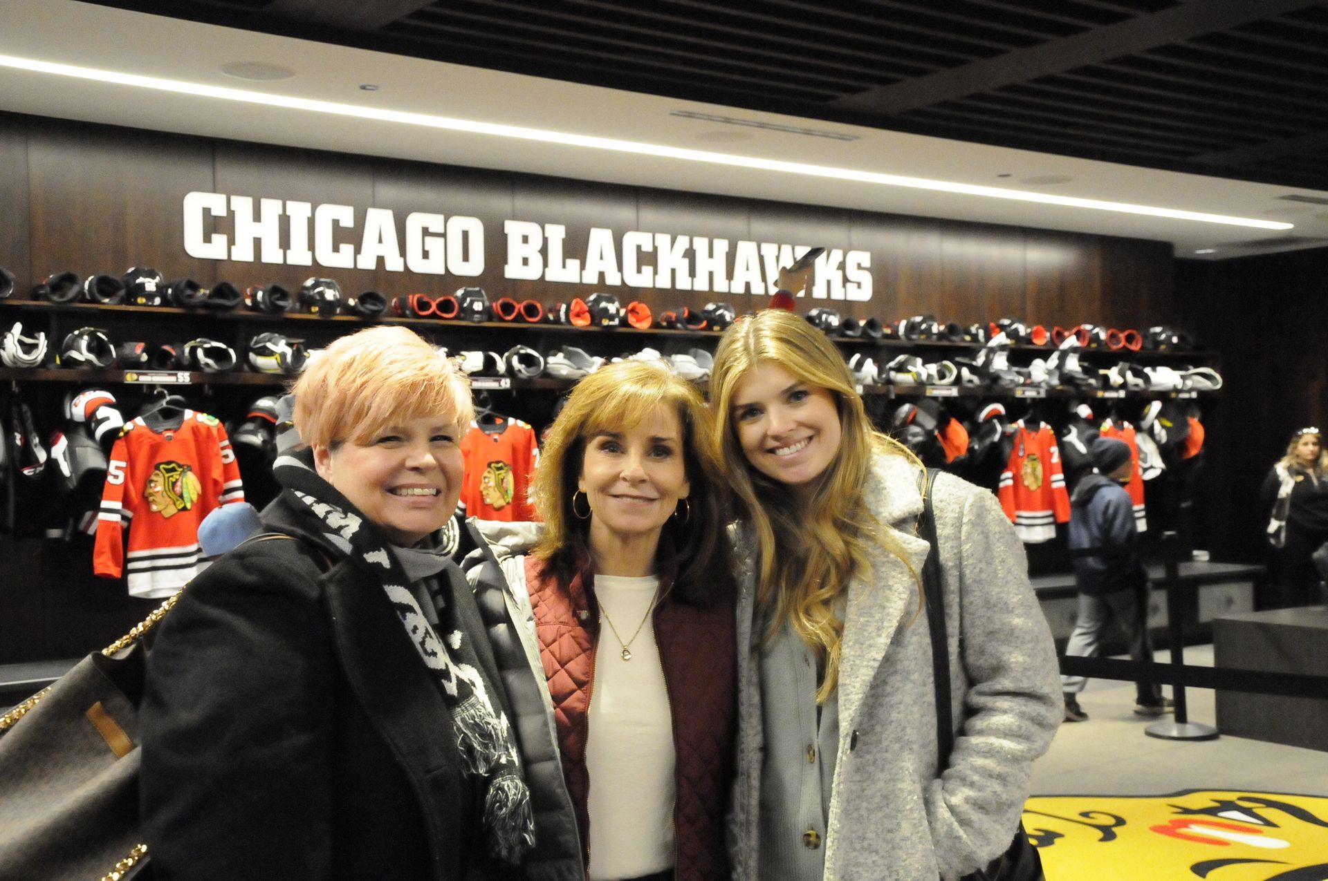 Three women are posing for a picture in front of a sign that says chicago blackhawks