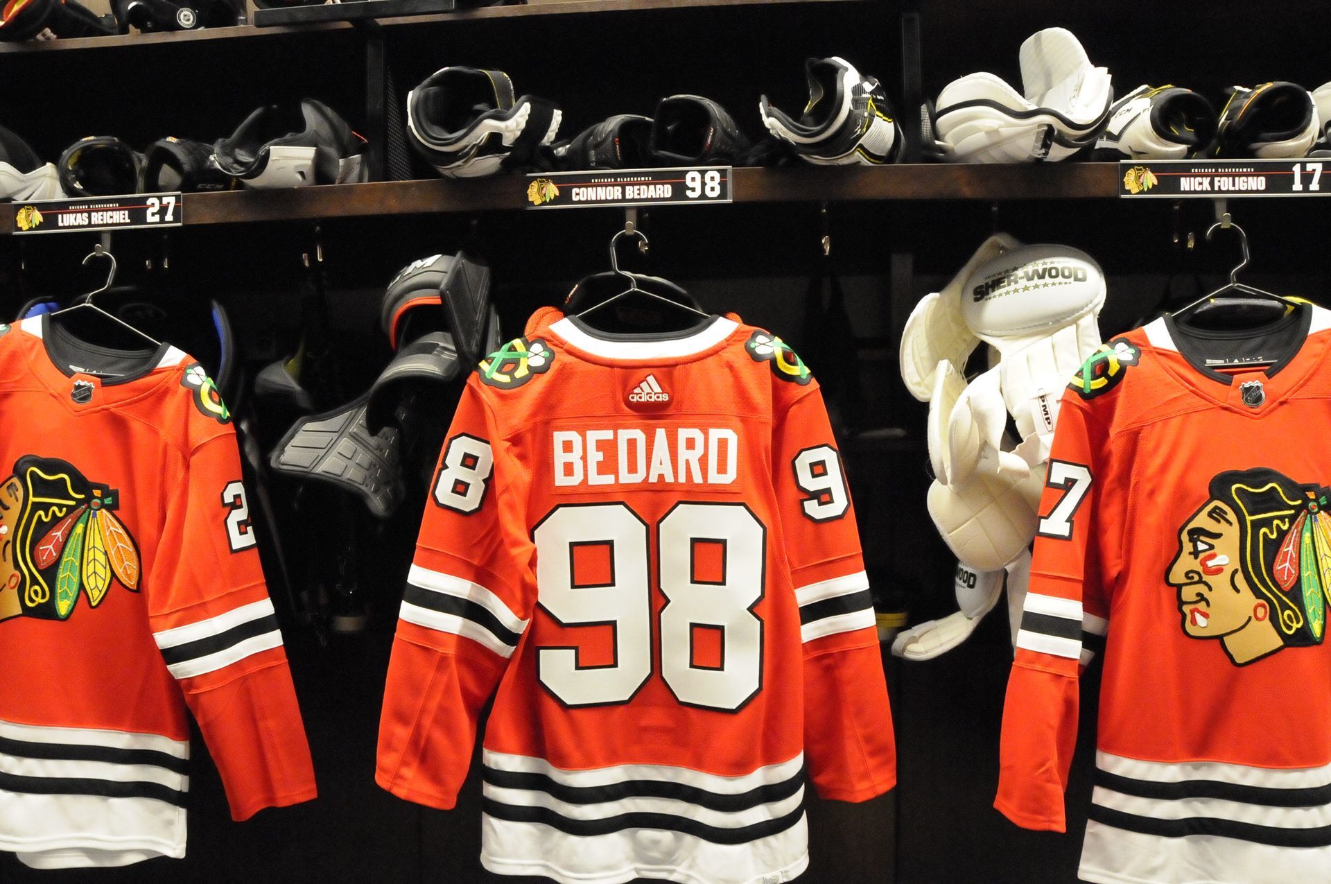 A hockey jersey with the number 98 on it is hanging in a locker room.