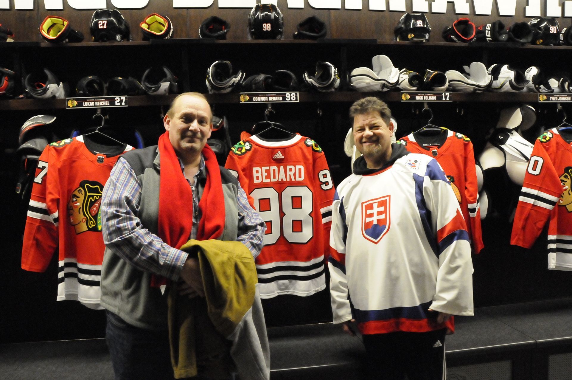 Two men standing in front of a hockey jersey with the number 98 on it