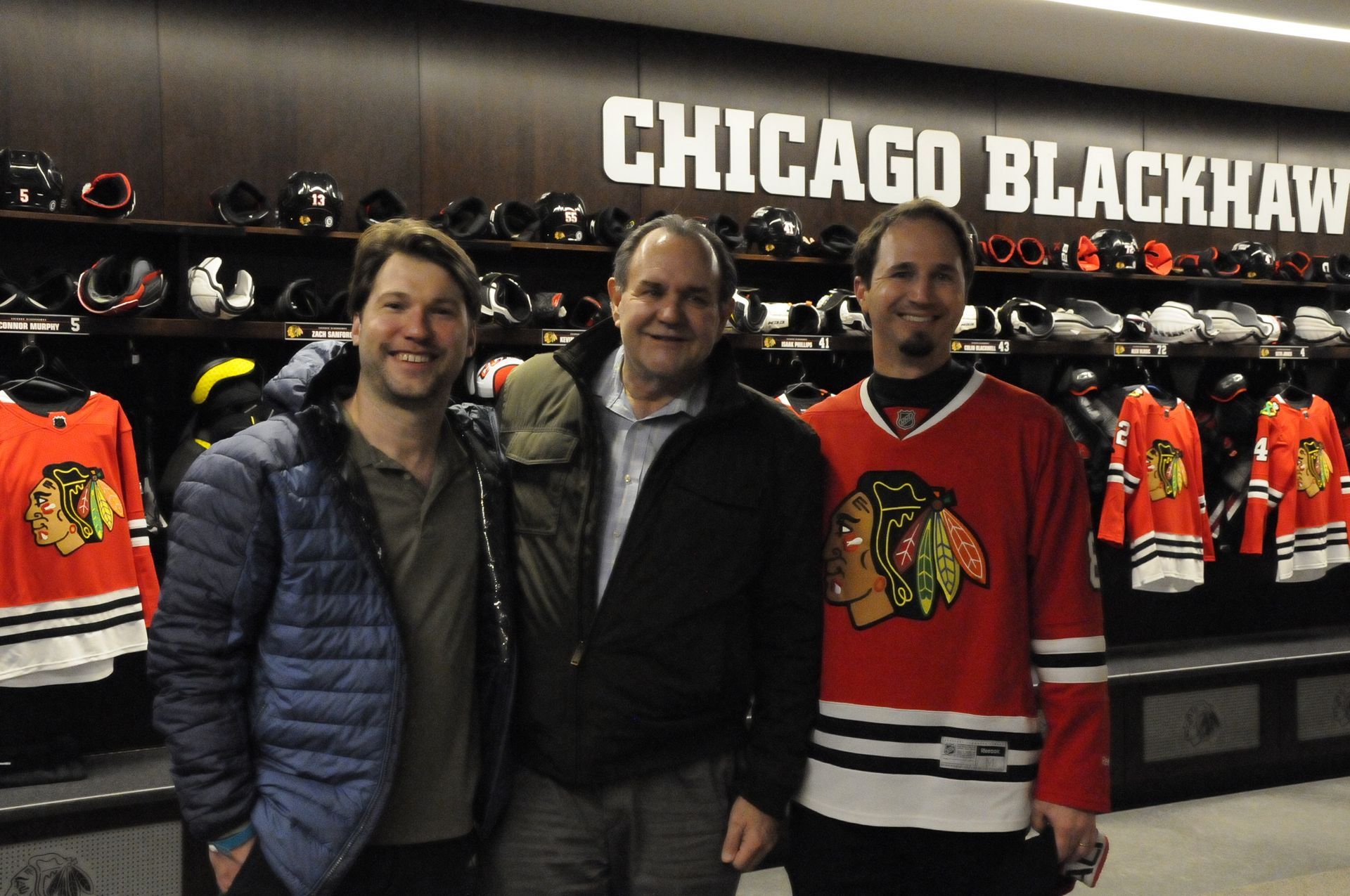 Three men are posing for a picture in front of a sign that says chicago blackhawks