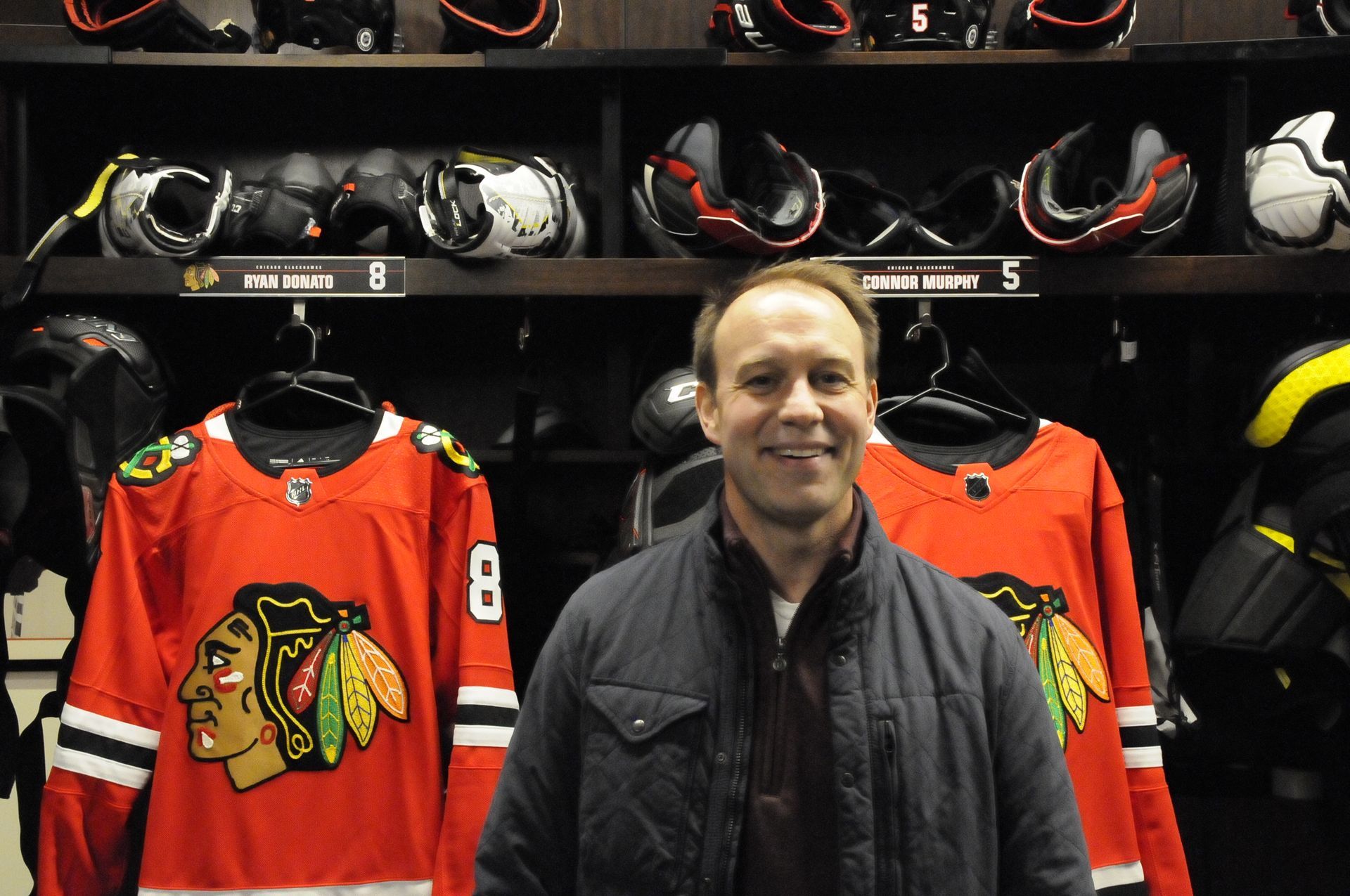 A man in a blackhawks jersey stands in a locker room