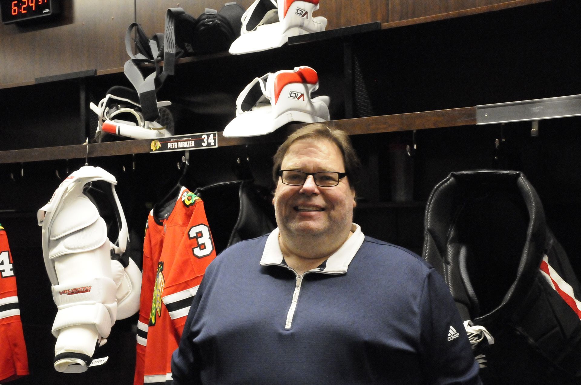 A man wearing glasses is standing in a hockey locker room