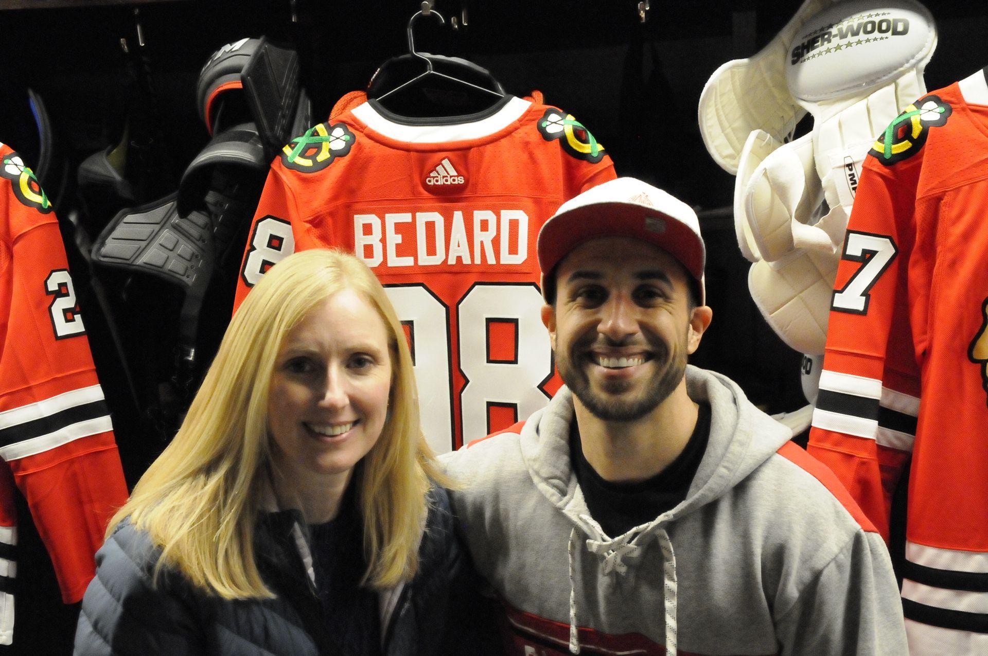 A man and a woman pose in front of a jersey that says bedard