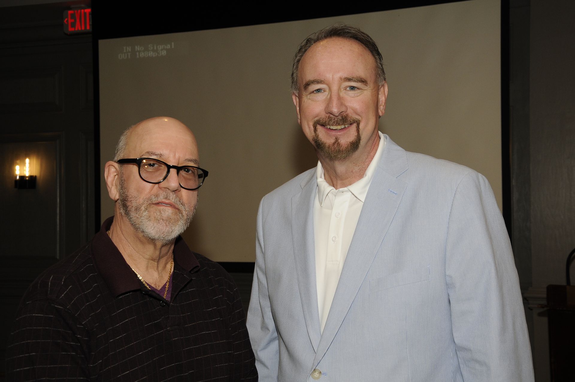 Two men are standing next to each other in front of a screen.