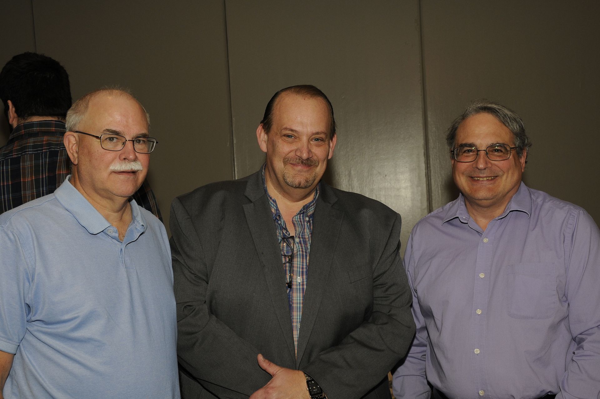 Three men are posing for a picture together in front of a wall.