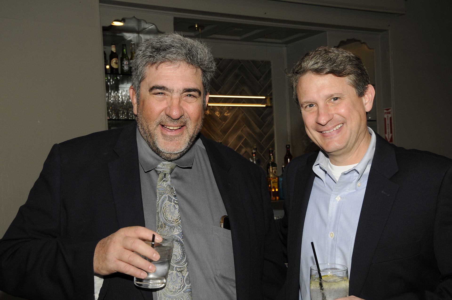 Two men in suits are posing for a picture while holding drinks.