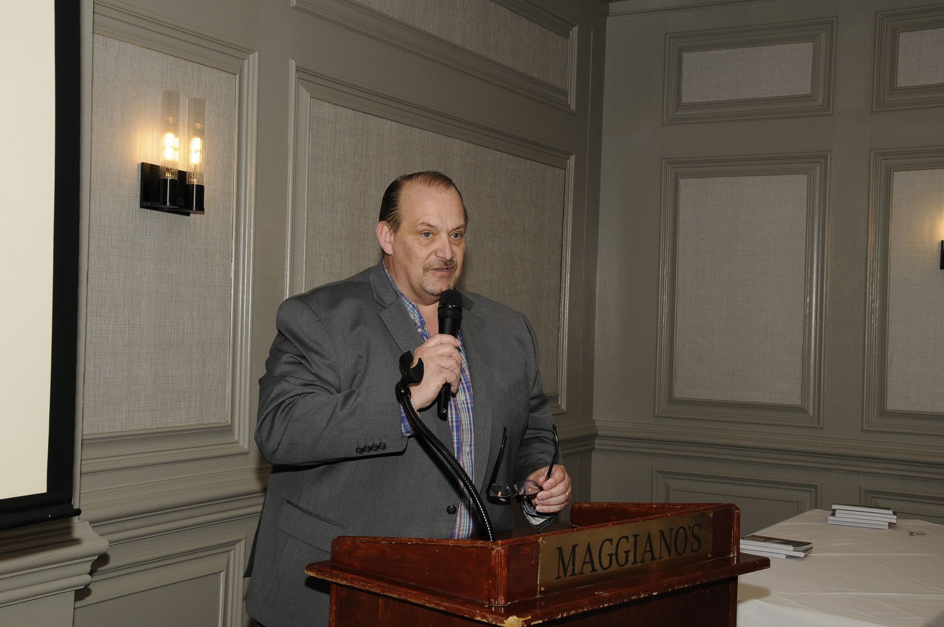 A man in a suit is standing at a podium holding a microphone.