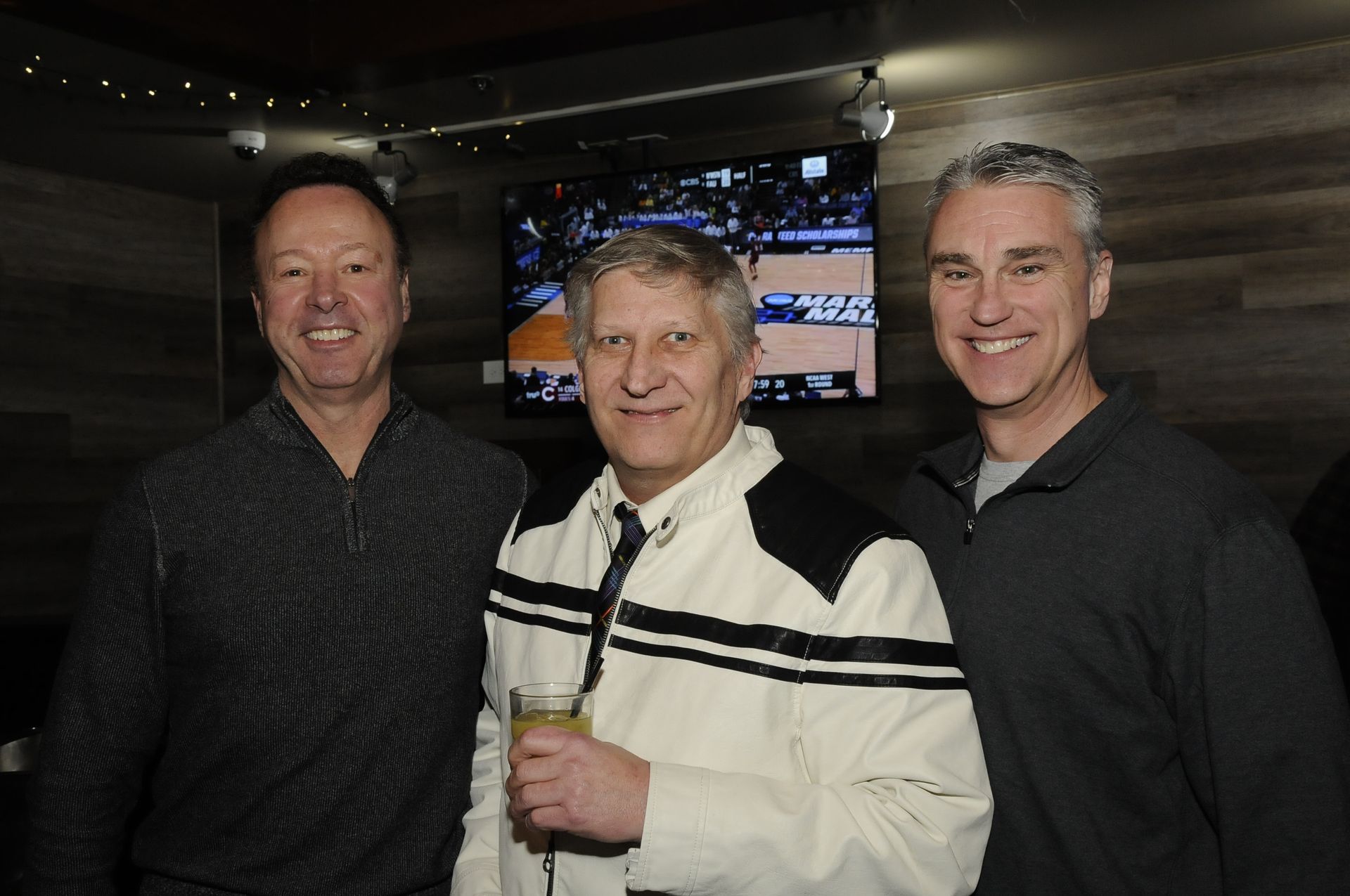 Three men are posing for a picture in front of a television.