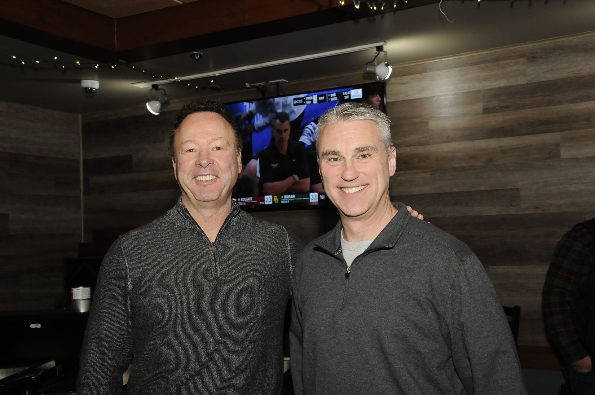 Two men are posing for a picture in front of a television.
