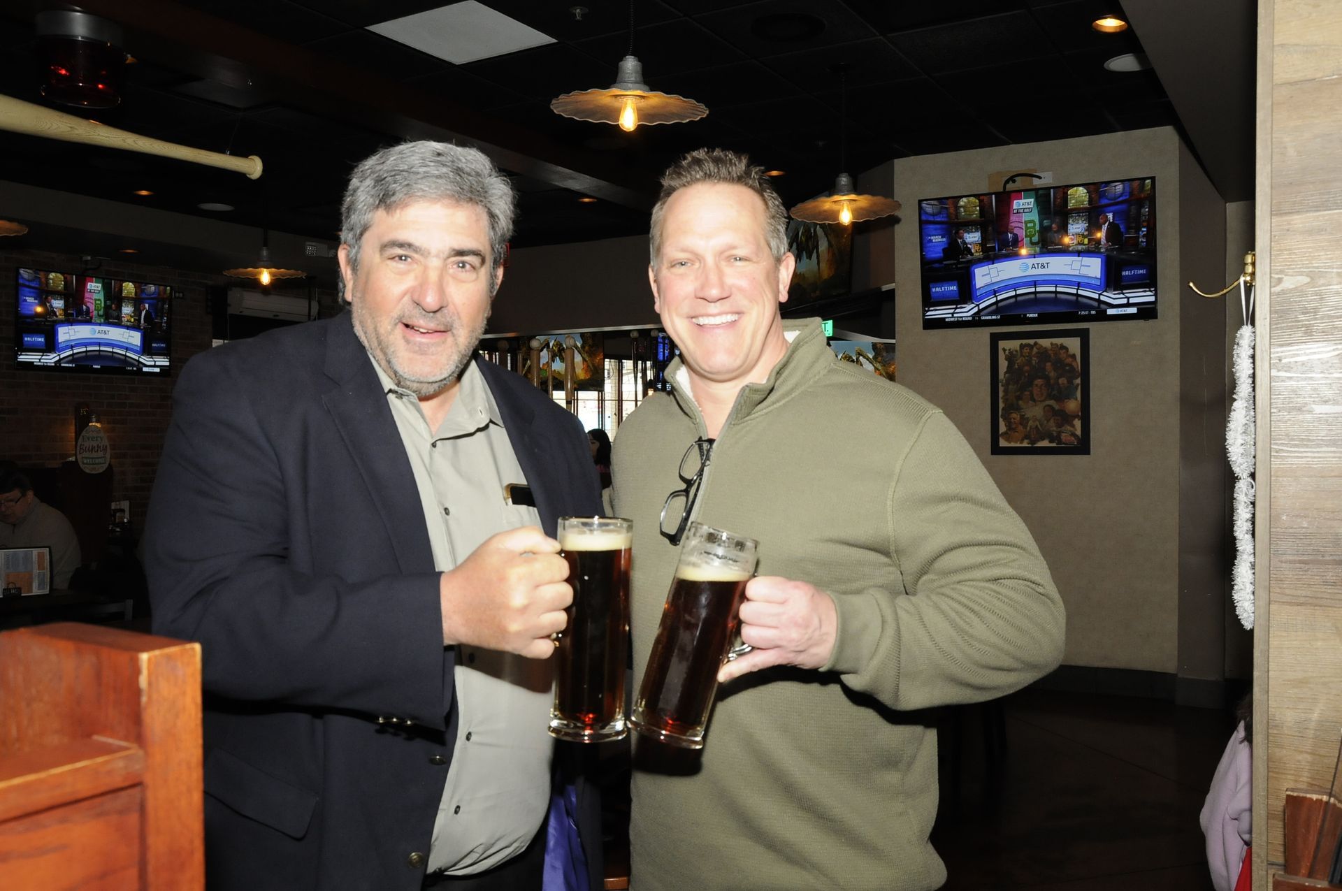 Two men are standing next to each other holding beer mugs in a bar.
