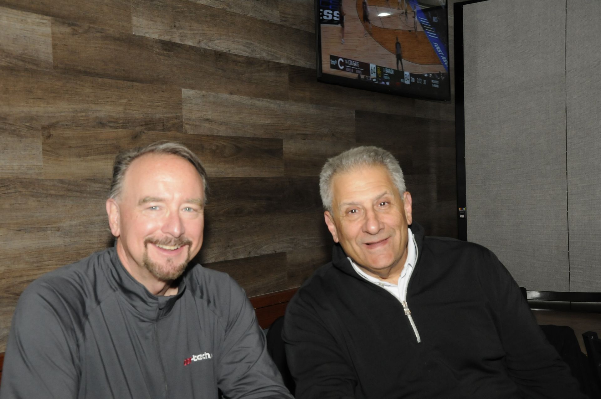 Two men are sitting next to each other in front of a television.